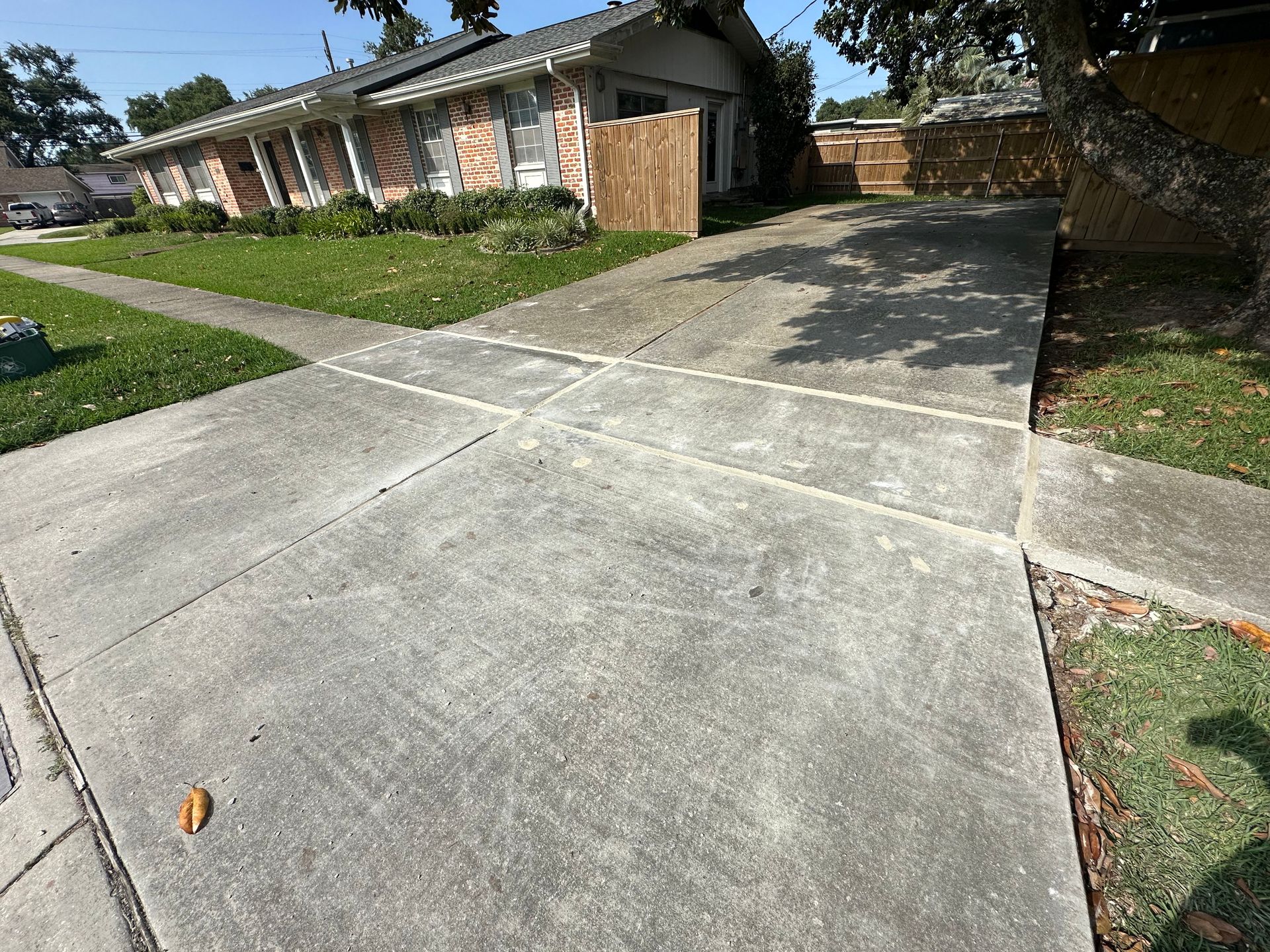 Concrete driveway leading to a house with a lawn and sidewalk on a sunny day.