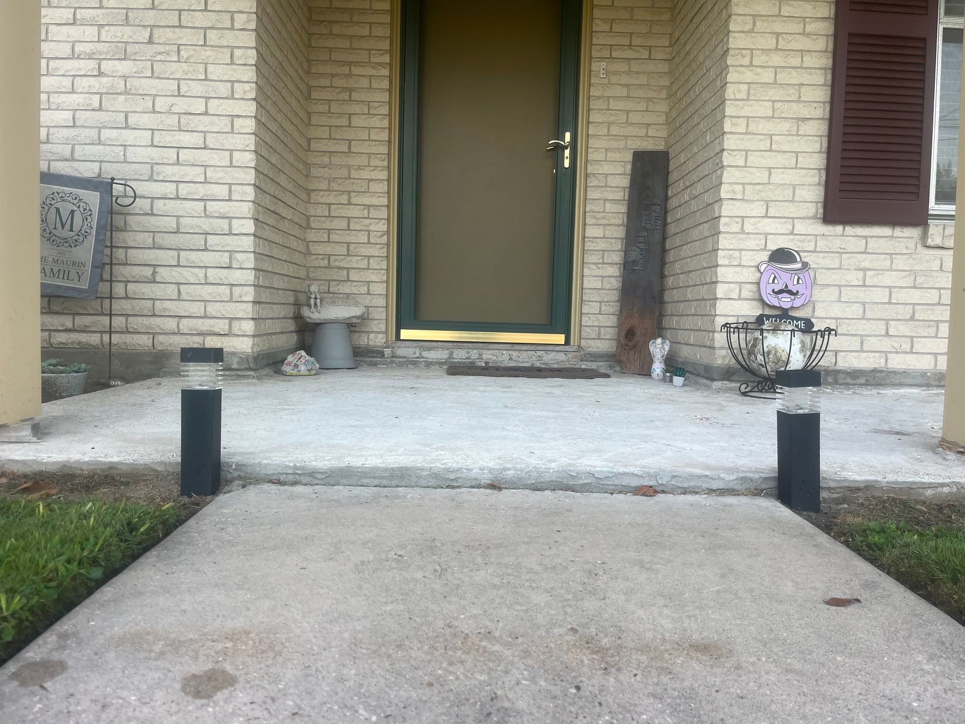 Concrete walkway leading to a front porch with a green door, flanked by brick columns and solar lights.