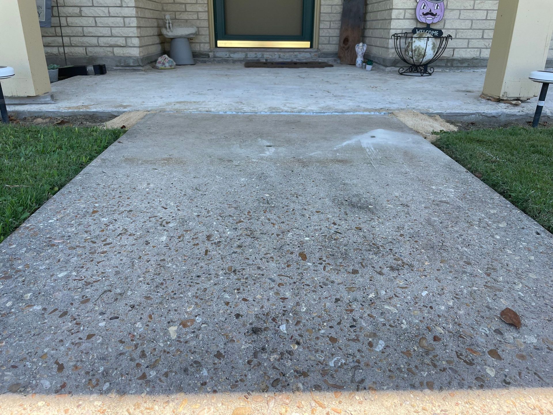 Concrete walkway leading to a building's entrance, flanked by grass, under a blue sky.
