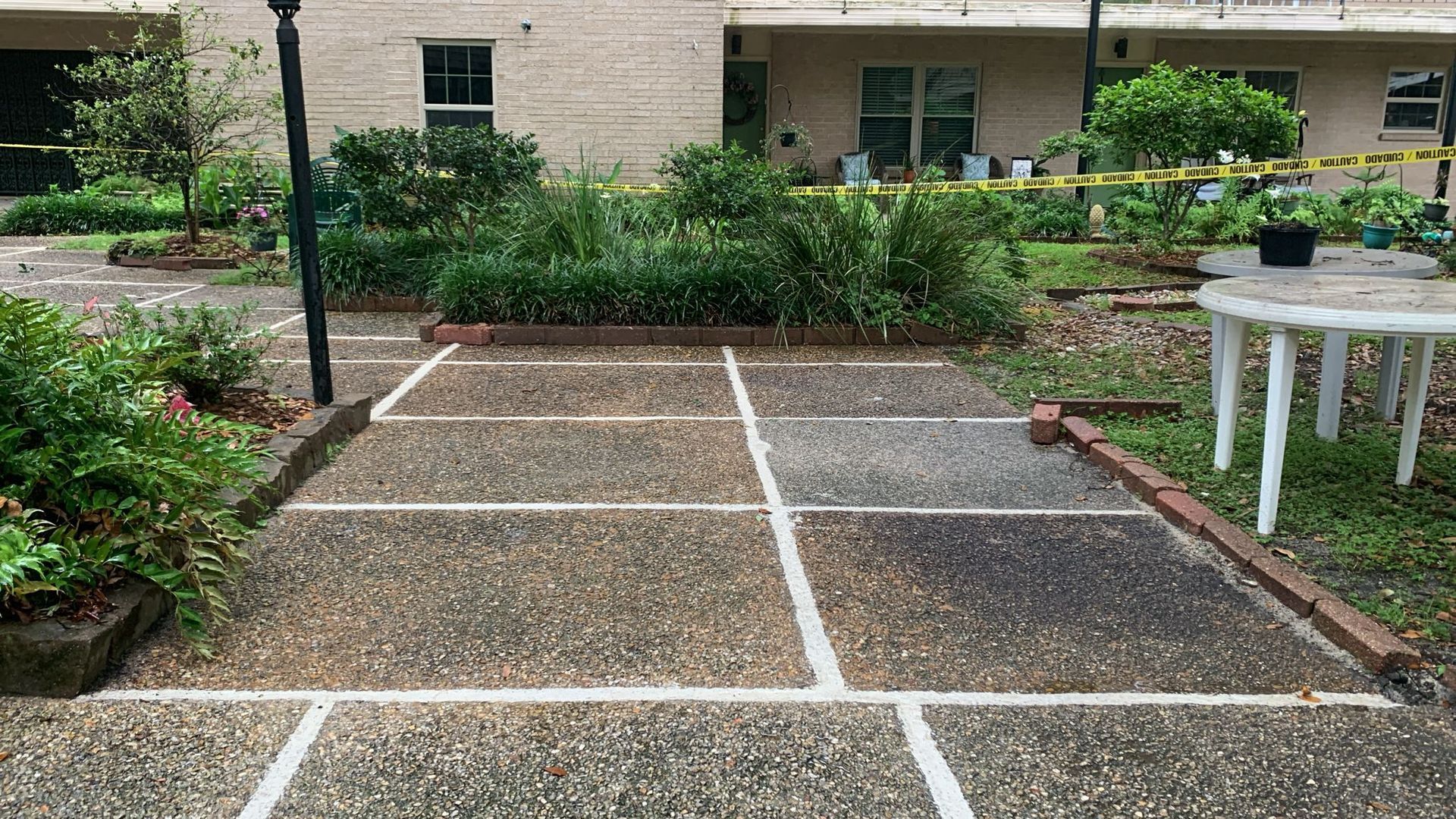 Paved courtyard with plants, a table, and a building in the background, yellow caution tape is seen.