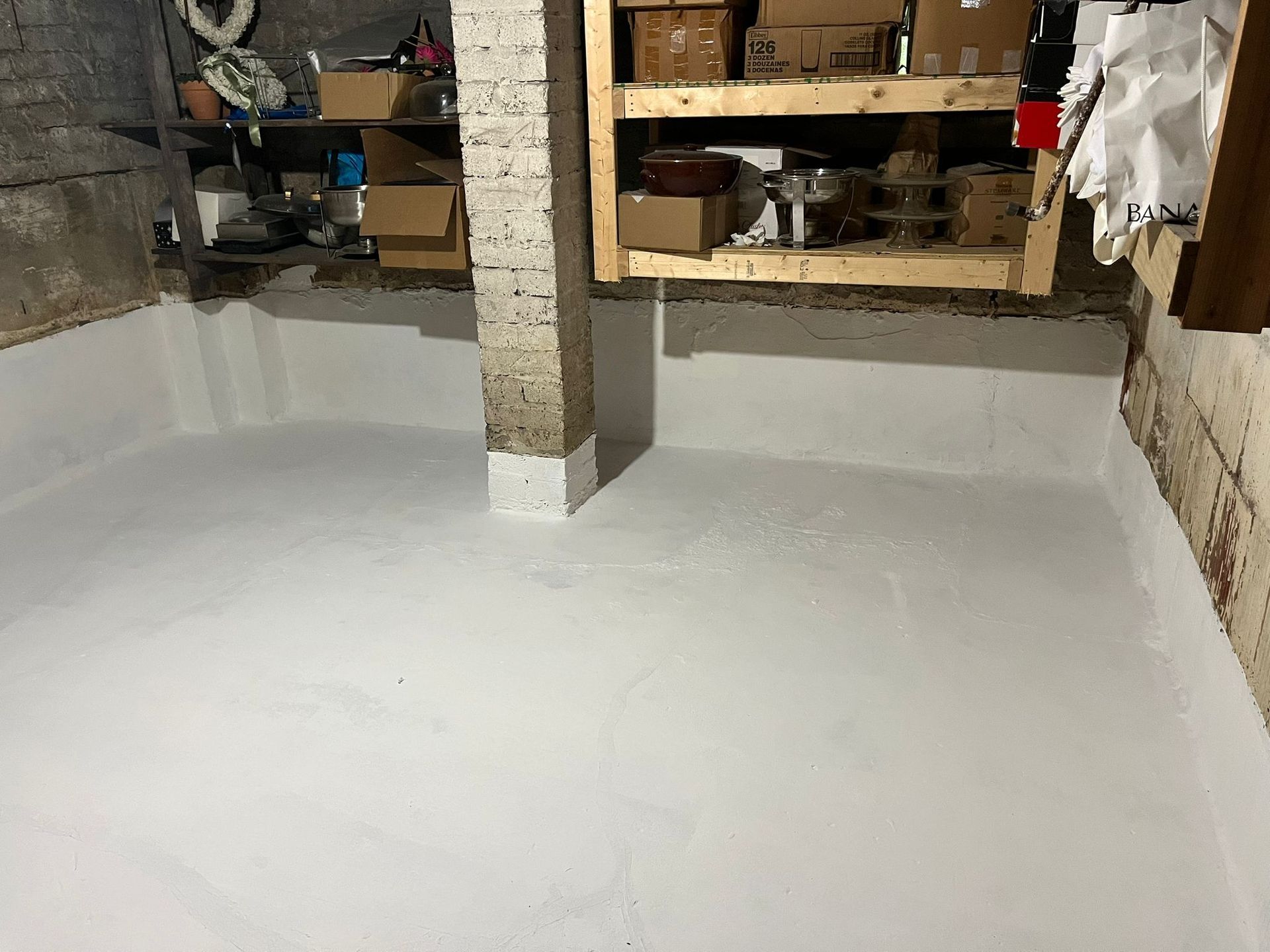 White-painted basement floor and walls; shelves with items in background.