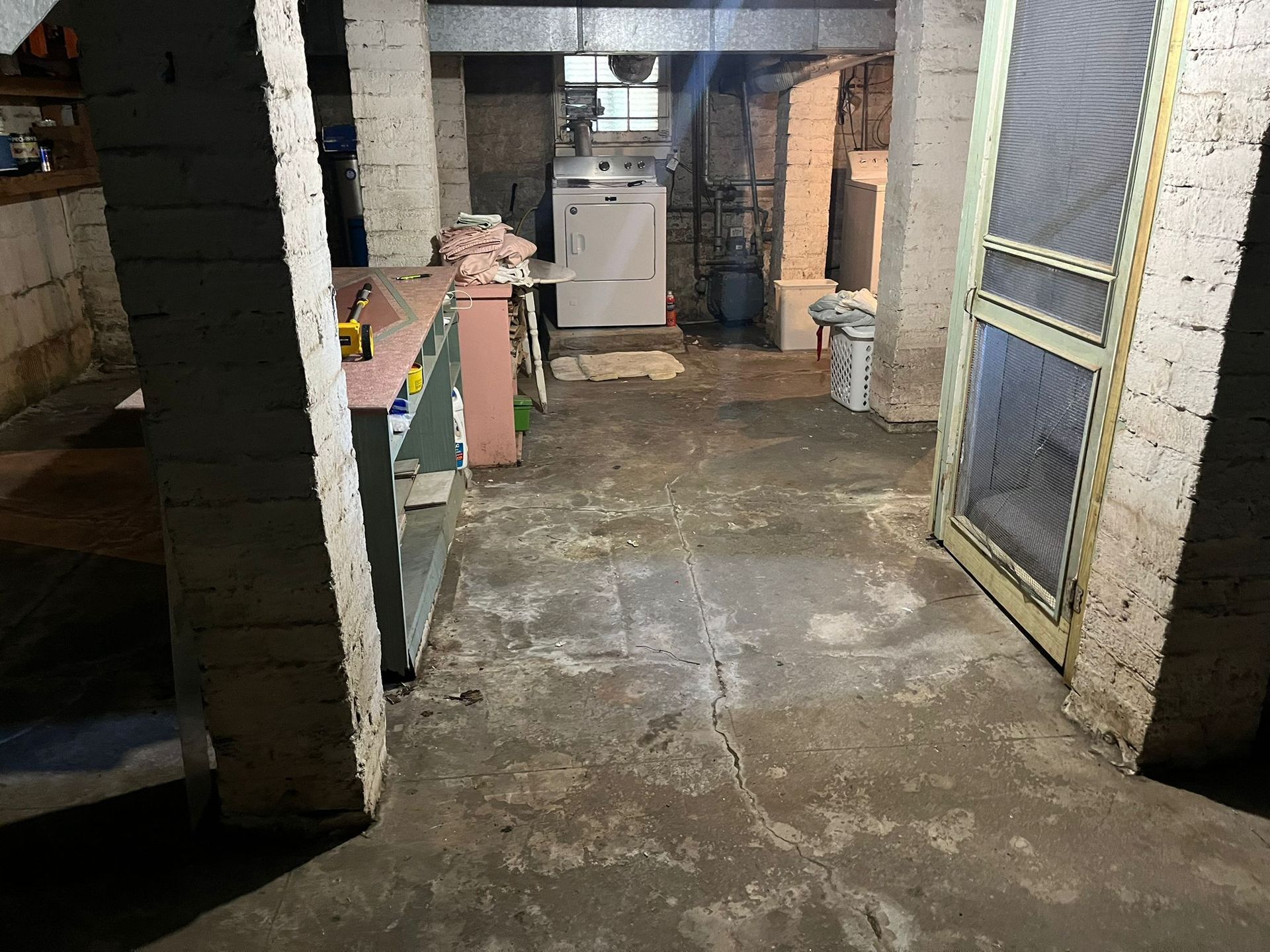 Basement interior with concrete floor, brick columns, workbench, laundry appliances.