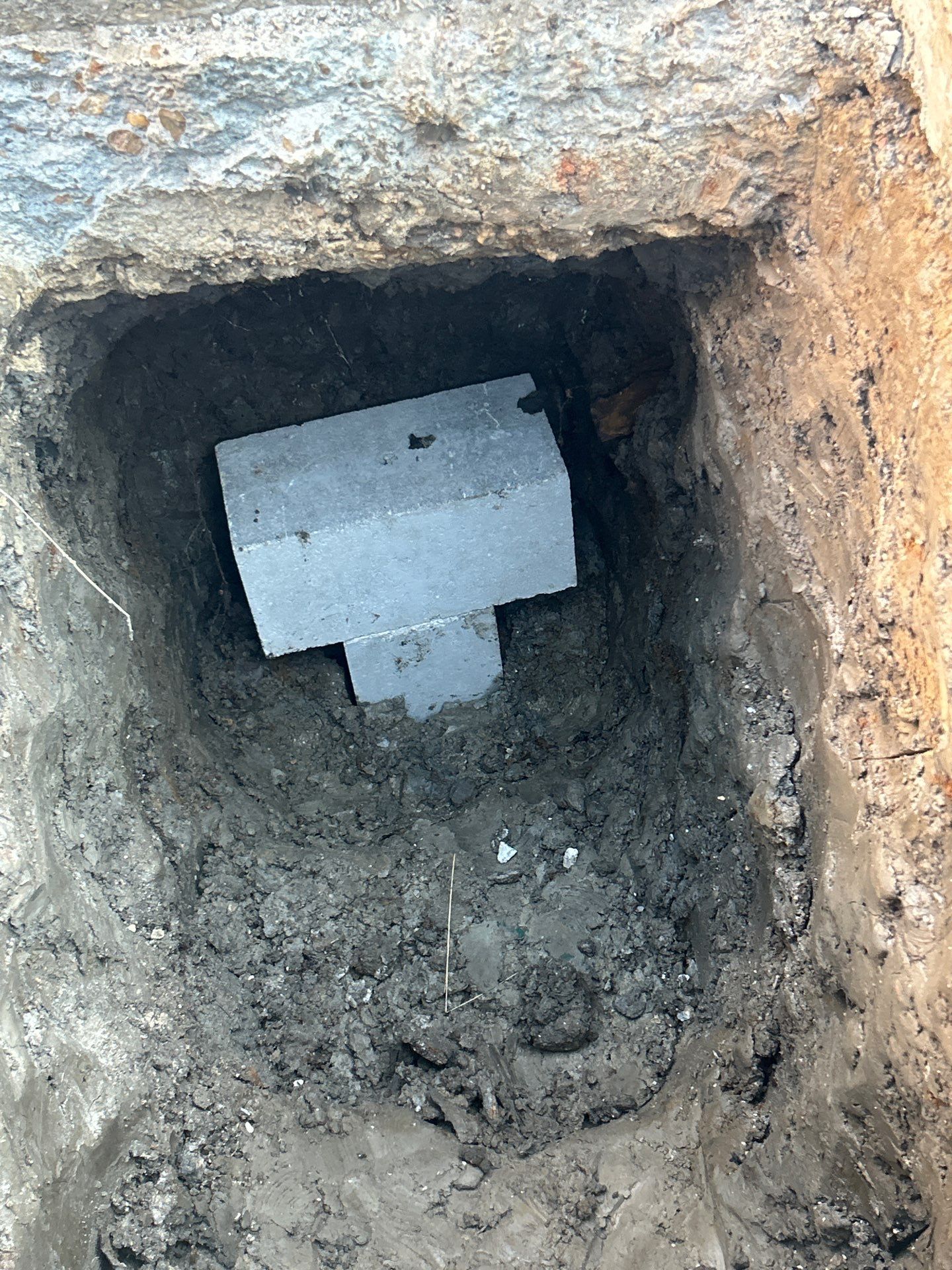 A square hole in the ground reveals a concrete structure with a 