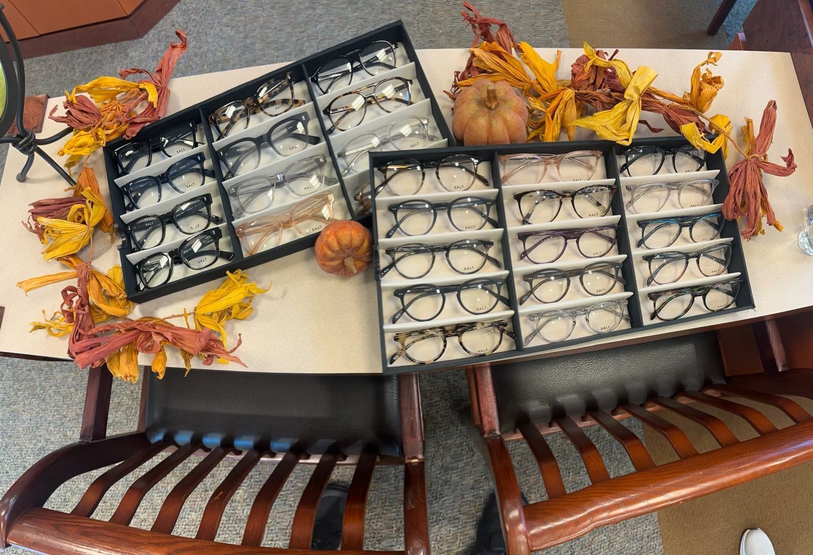 Two open display cases of eyeglasses on a table with autumn leaf decorations