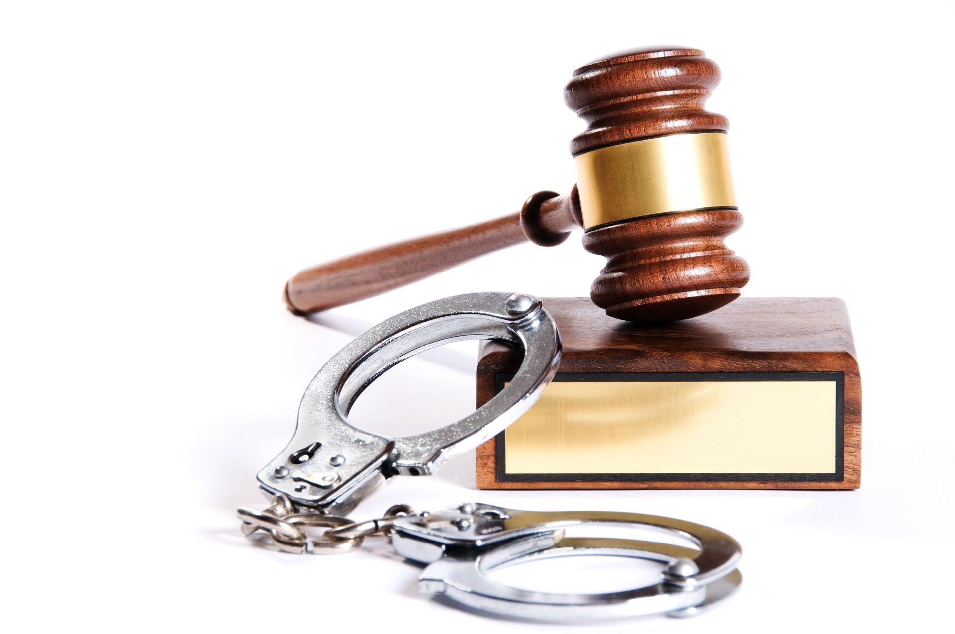 A wooden judge's gavel resting on a blank nameplate block next to a pair of metal handcuffs.
