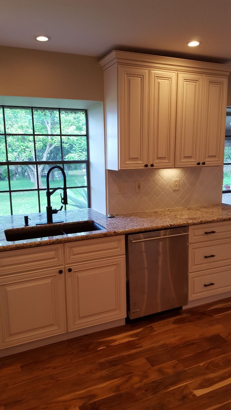 A kitchen with white cabinets , a sink , and a stainless steel dishwasher.