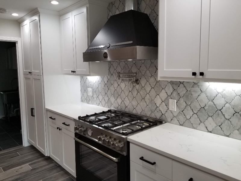 A kitchen with white cabinets , a stove , and a black hood.
