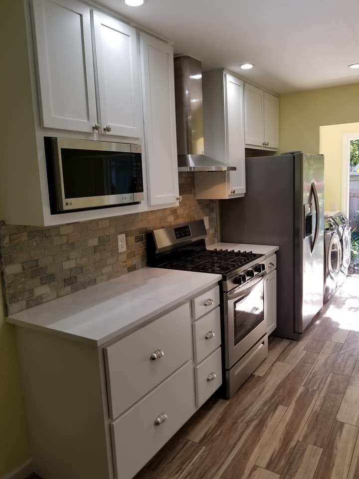 A kitchen with white cabinets , a stove , a refrigerator , and a microwave.