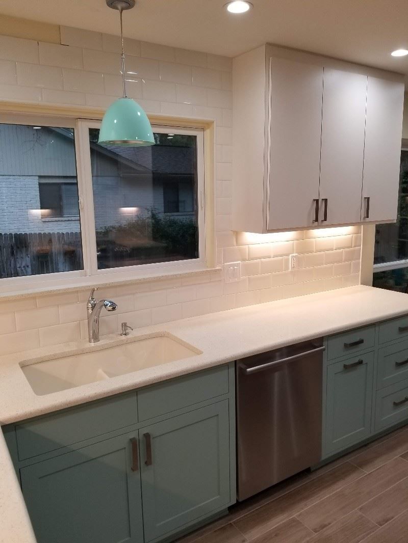 A kitchen with blue cabinets , stainless steel appliances , a sink and a window.