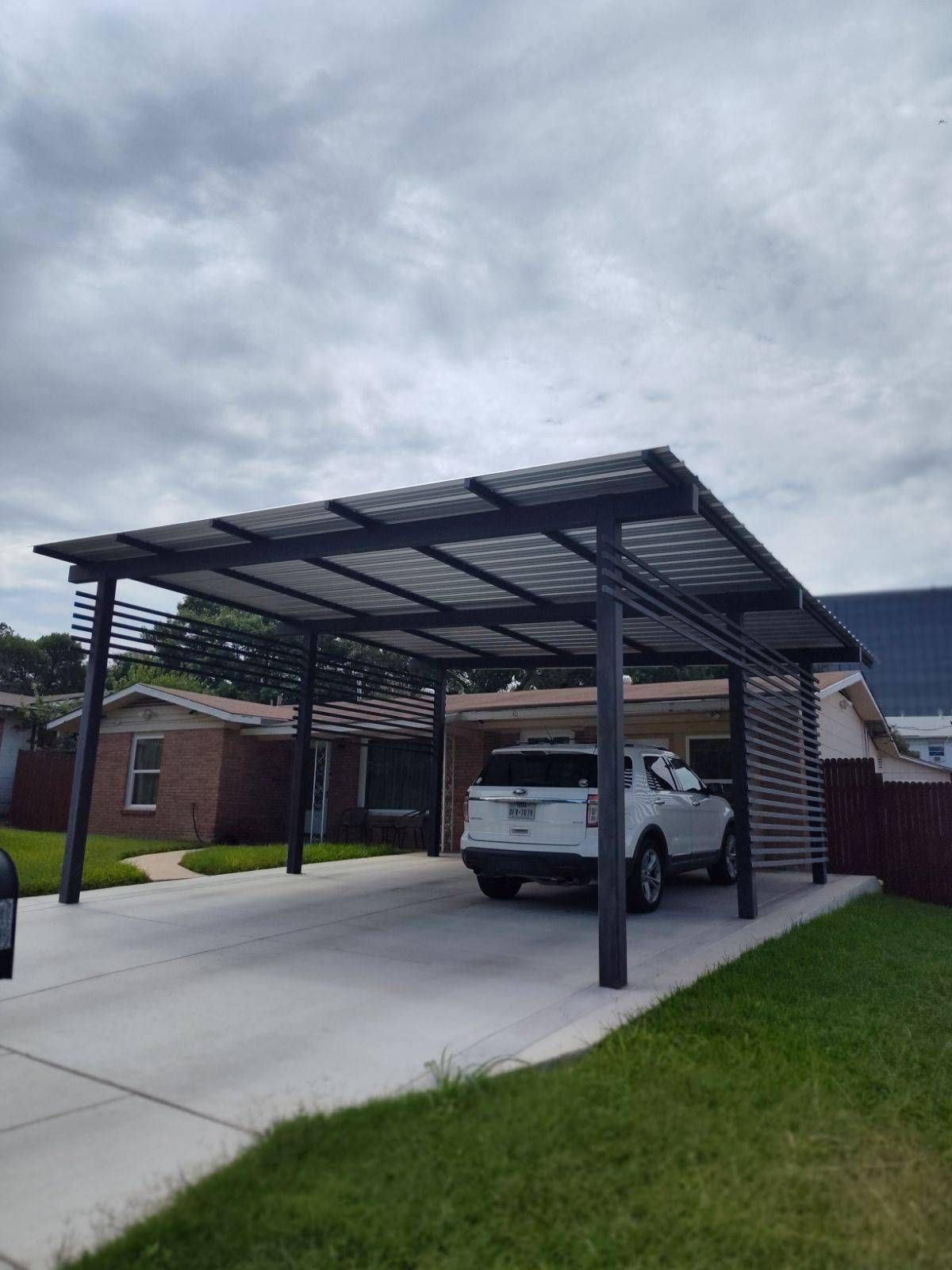 A car is parked under a carport in front of a house.