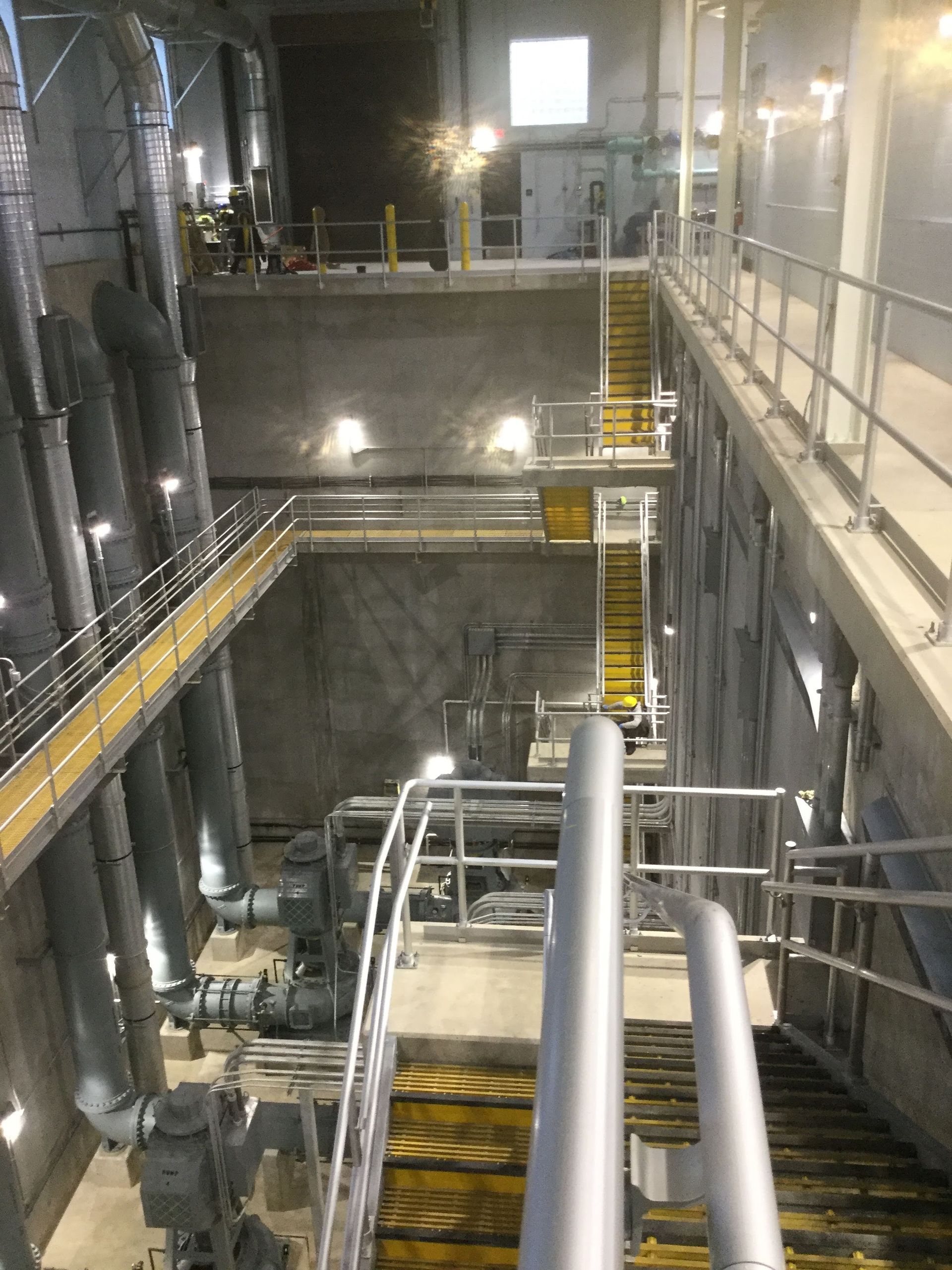 Long vertical view inside an industrial building, with pipes, stairs, and catwalks.