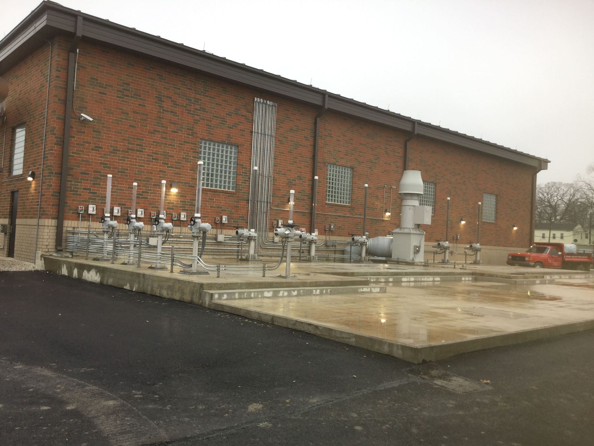 Brick building with industrial piping and equipment on a concrete pad. Wet, overcast day.