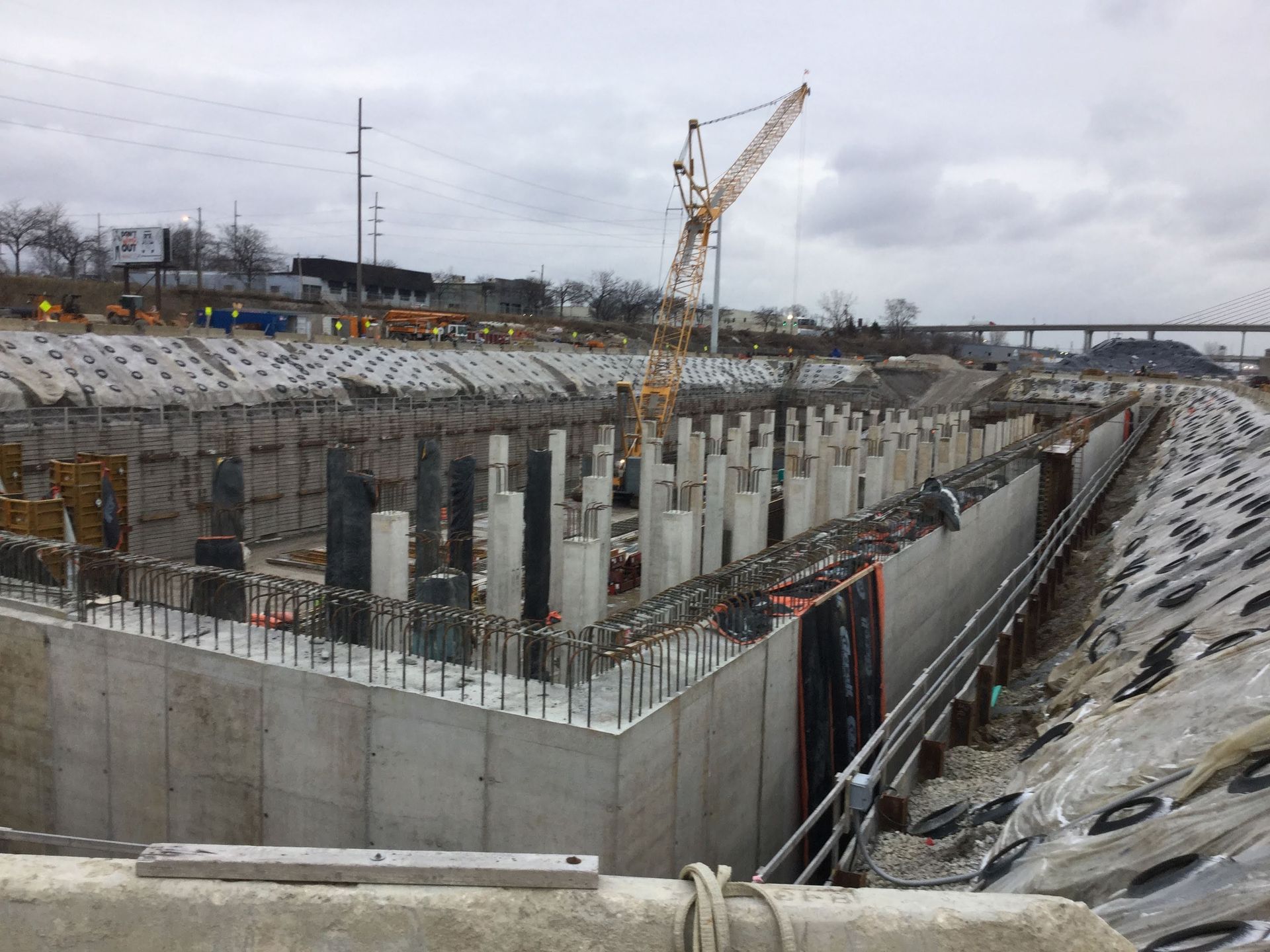 Construction site: Concrete structure with rebar and support pillars, crane in the background.