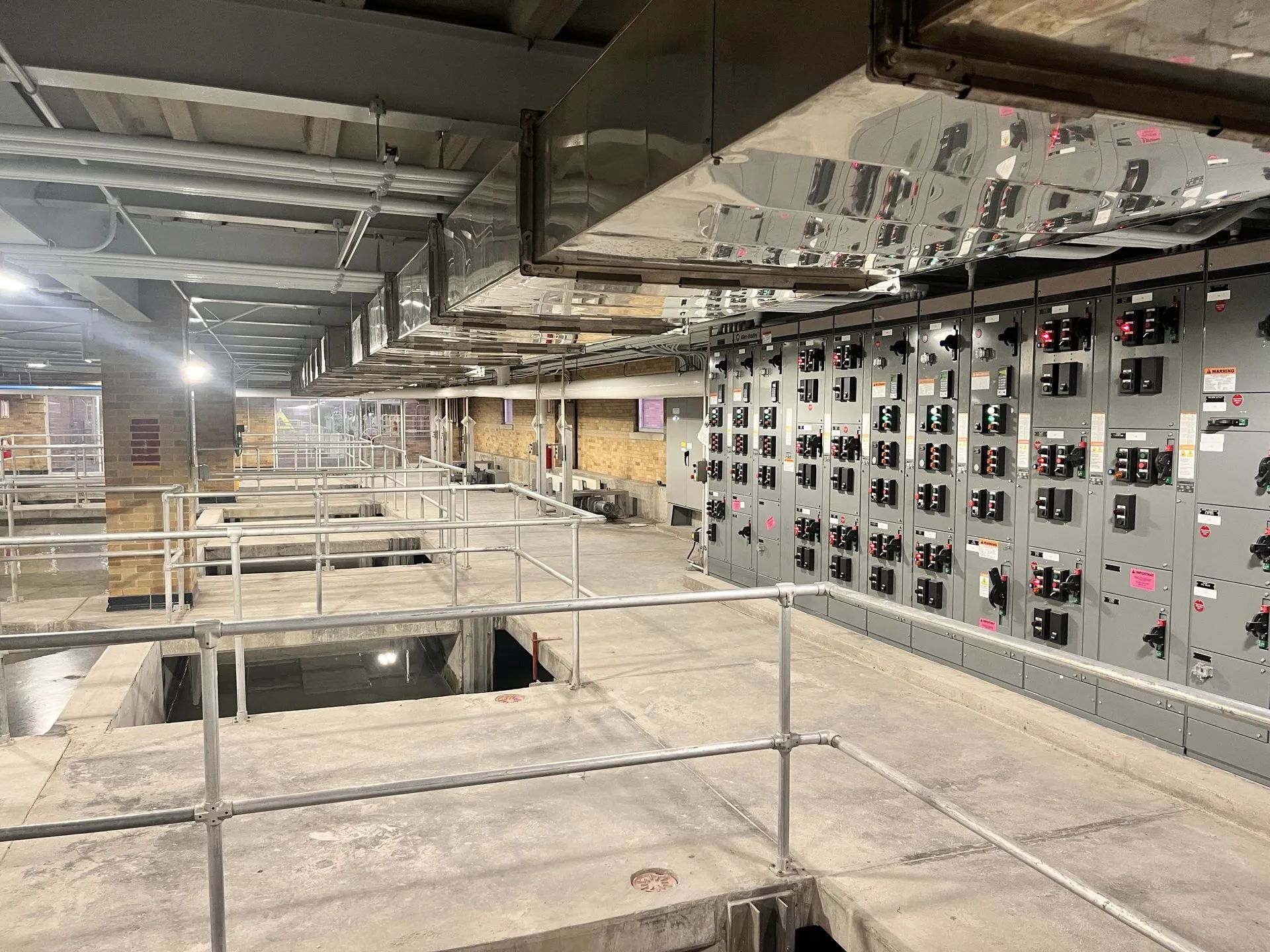 A large industrial room with machinery and control panels. Concrete walkways with railings.