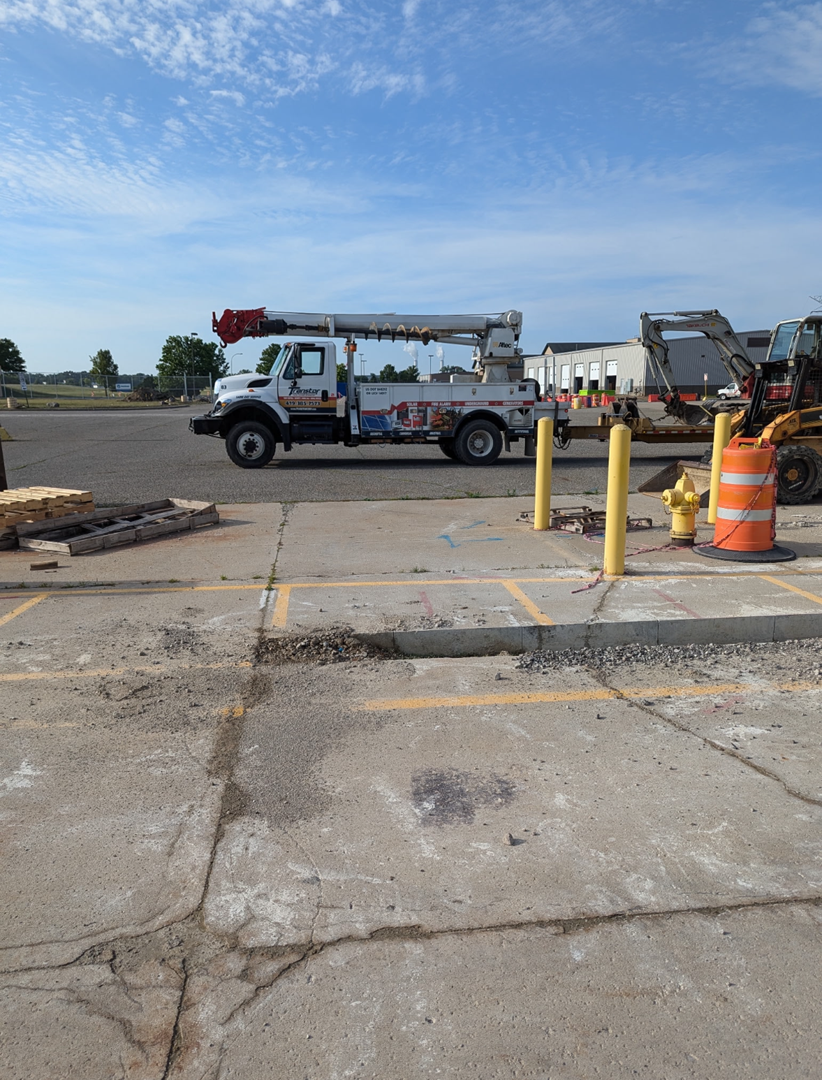 Utility truck with extended boom parked in a construction area, orange traffic cone, cloudy sky.