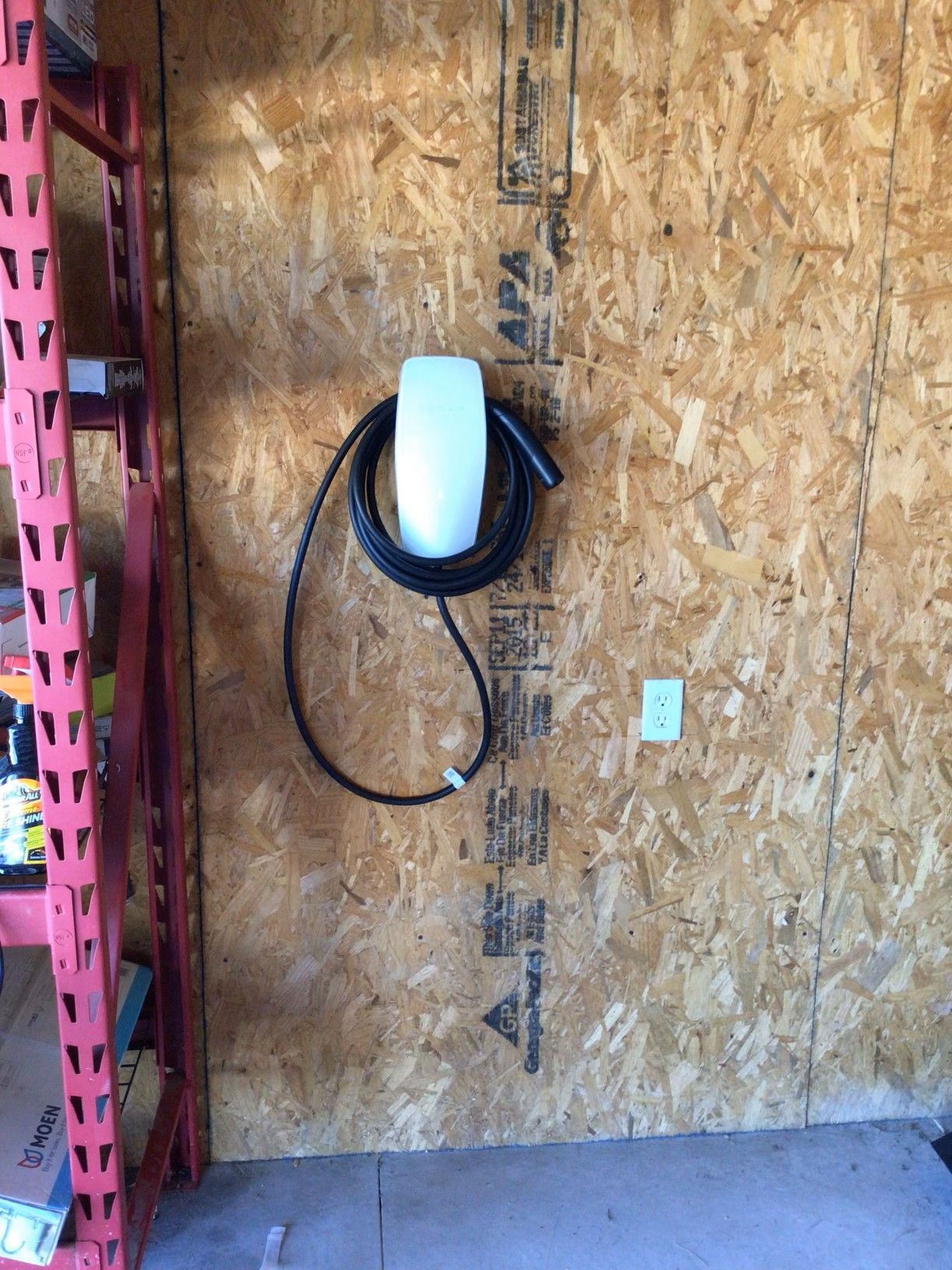A tesla charging station is hanging on a wooden wall in a garage.