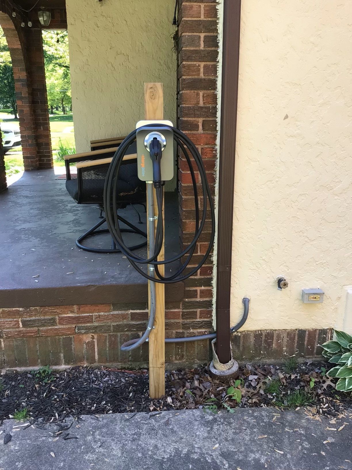 A charger is attached to a wooden post on the side of a building.