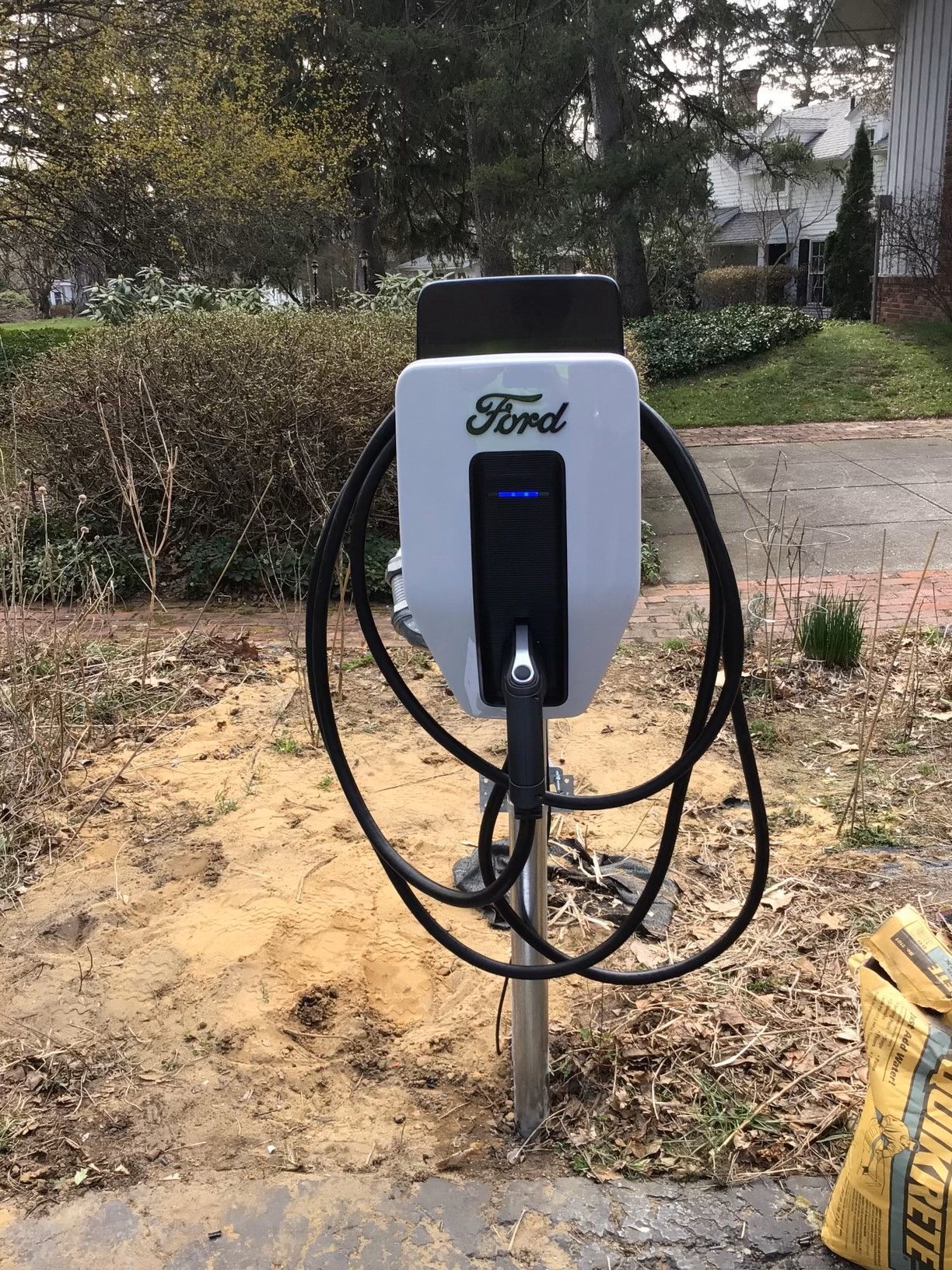A ford electric car charging station is sitting in the dirt in front of a house.