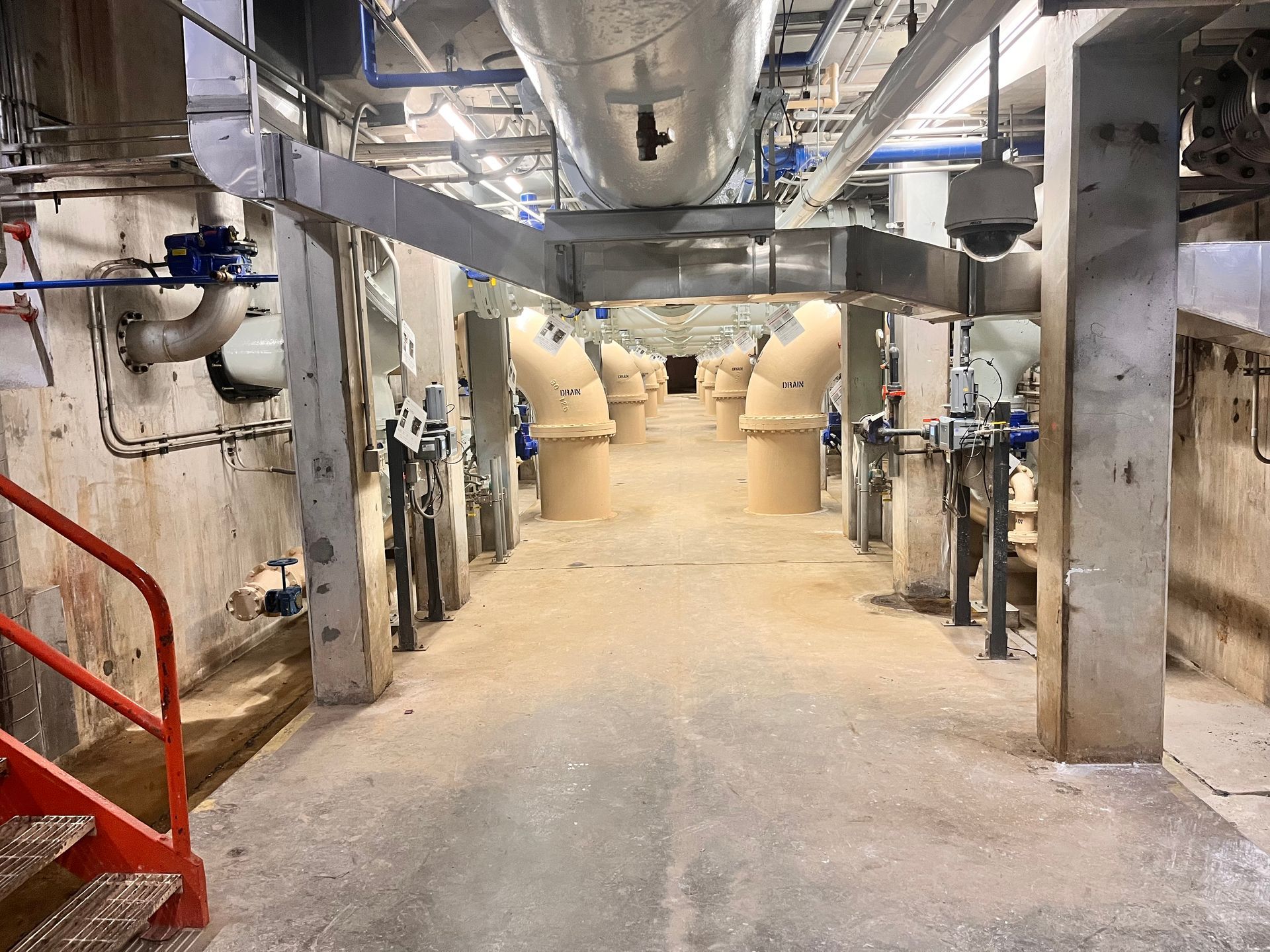 Inside of a utility room: concrete floor and walls, large pipes, valves, and equipment.