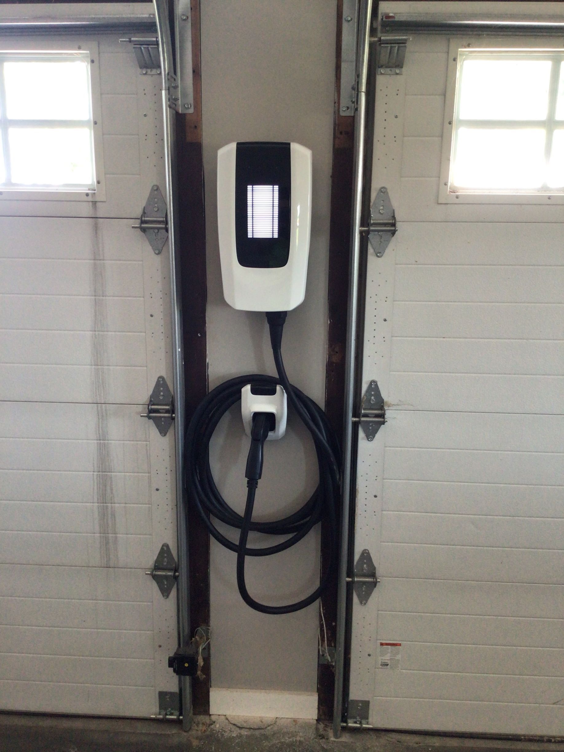 An electric car charger is attached to the side of a garage door.