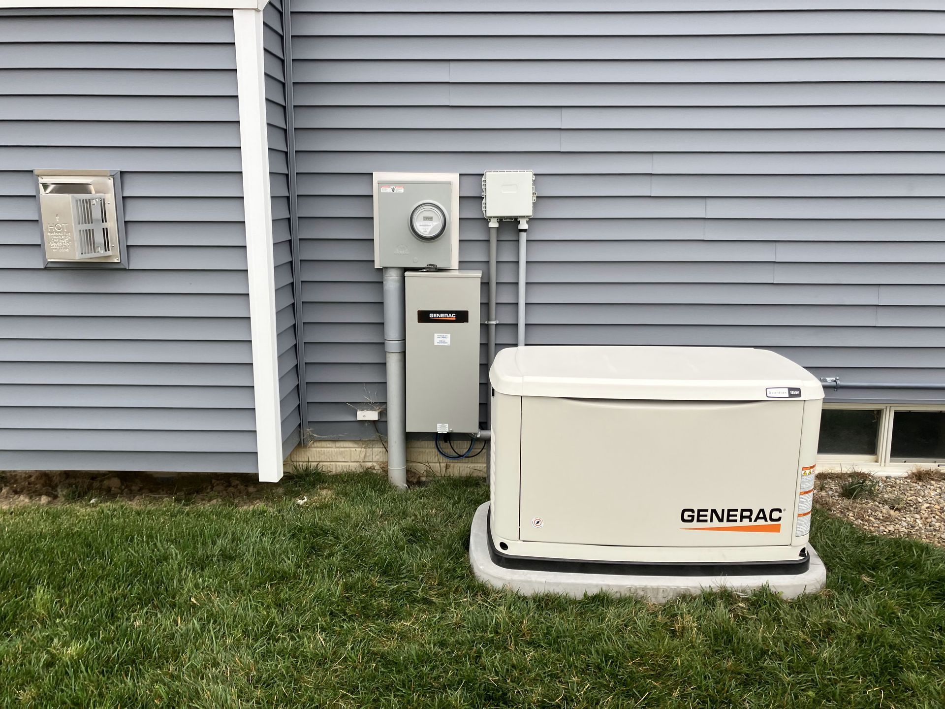 A generator is sitting in the grass next to a house.