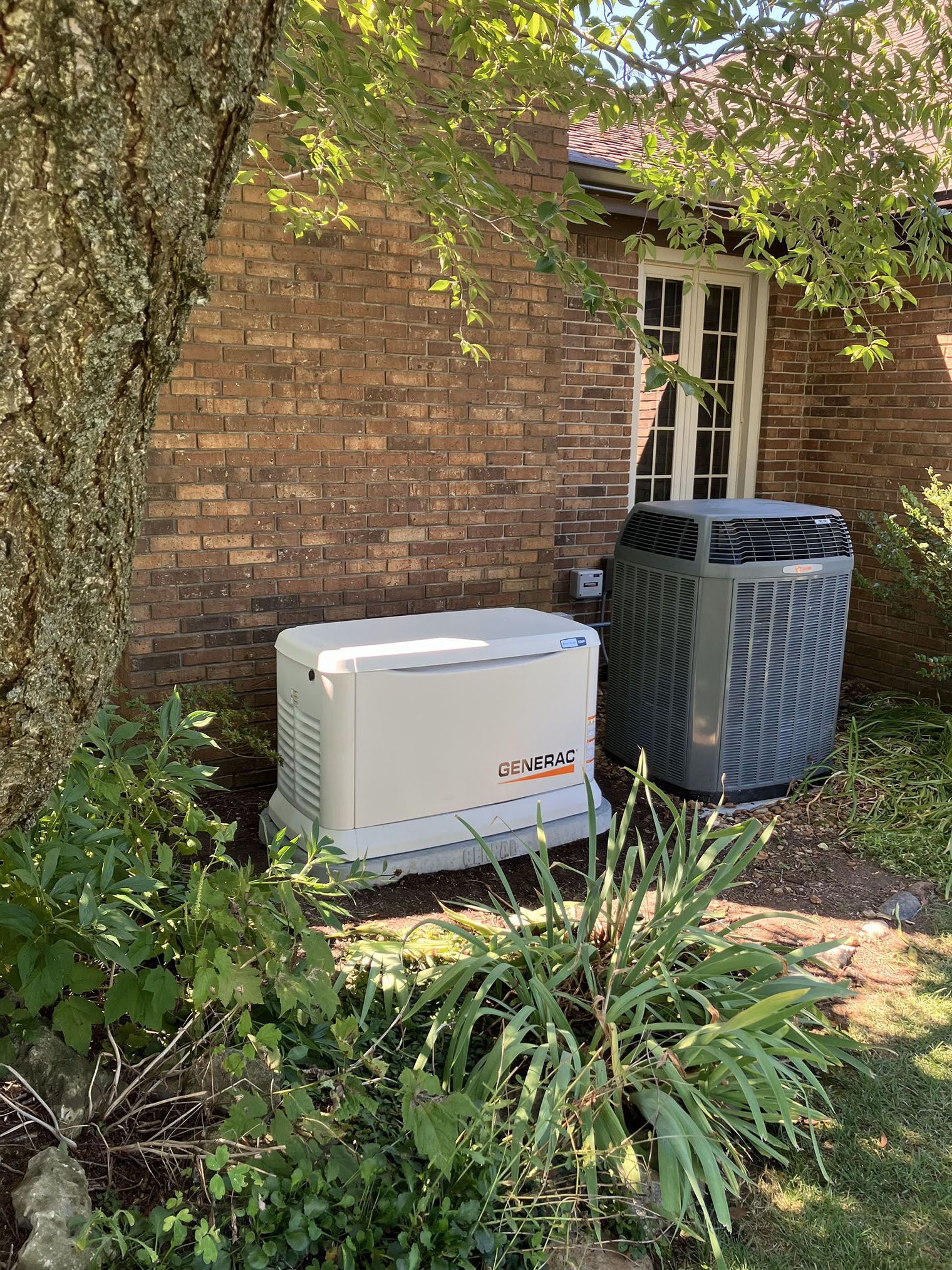 A brick house with a generator and air conditioner in the backyard.