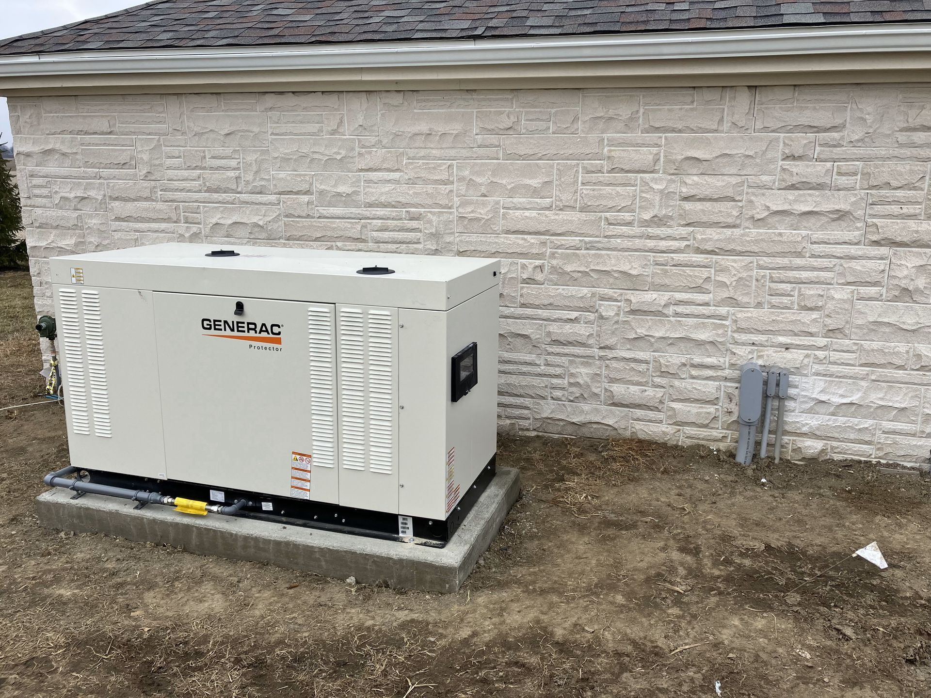 A generator is sitting on the side of a brick building.