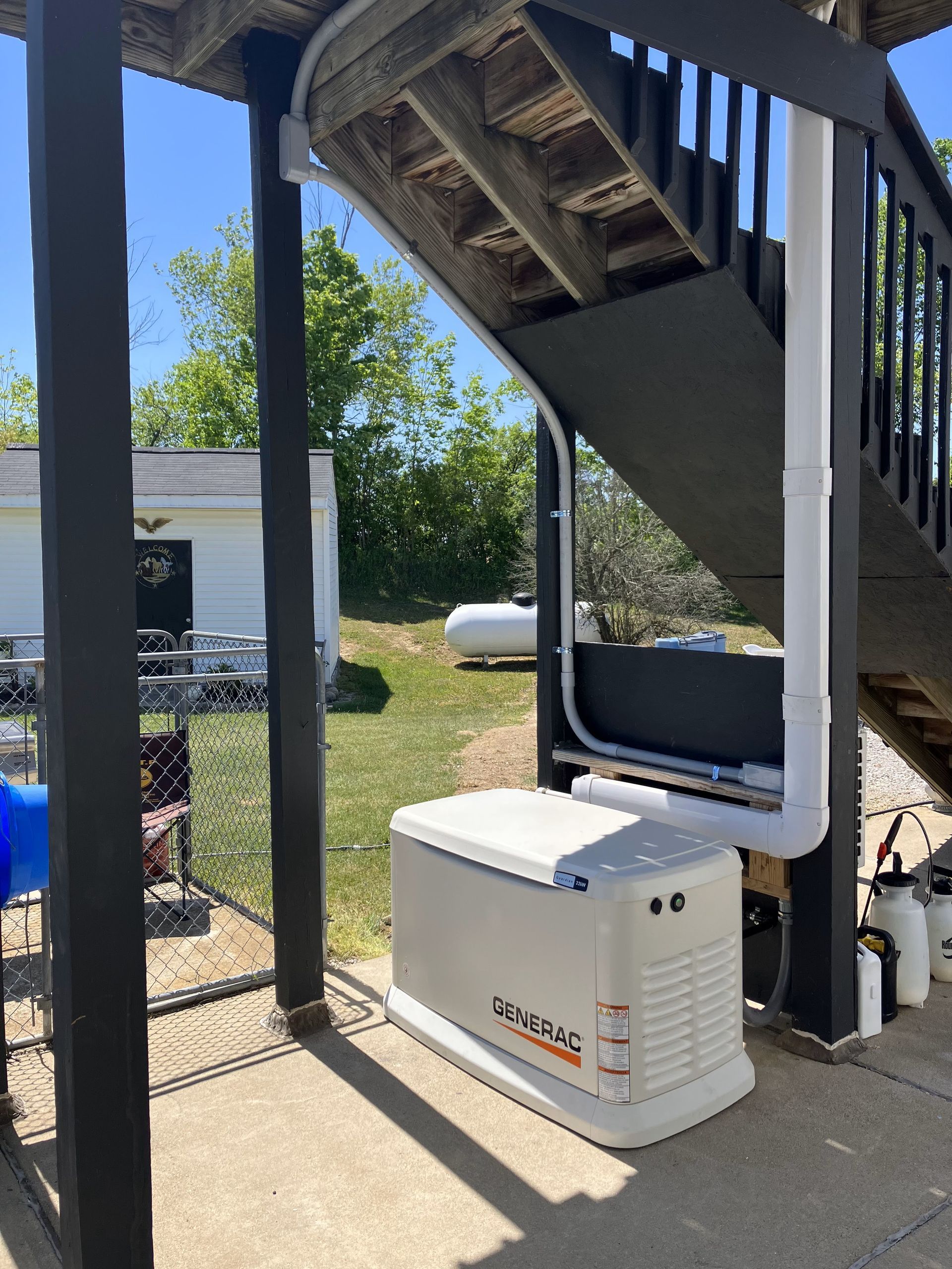 A generator is sitting under a staircase in a backyard.
