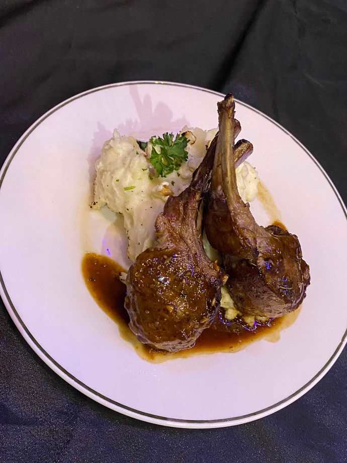 Lamb chops with mashed potatoes and gravy on a white plate.