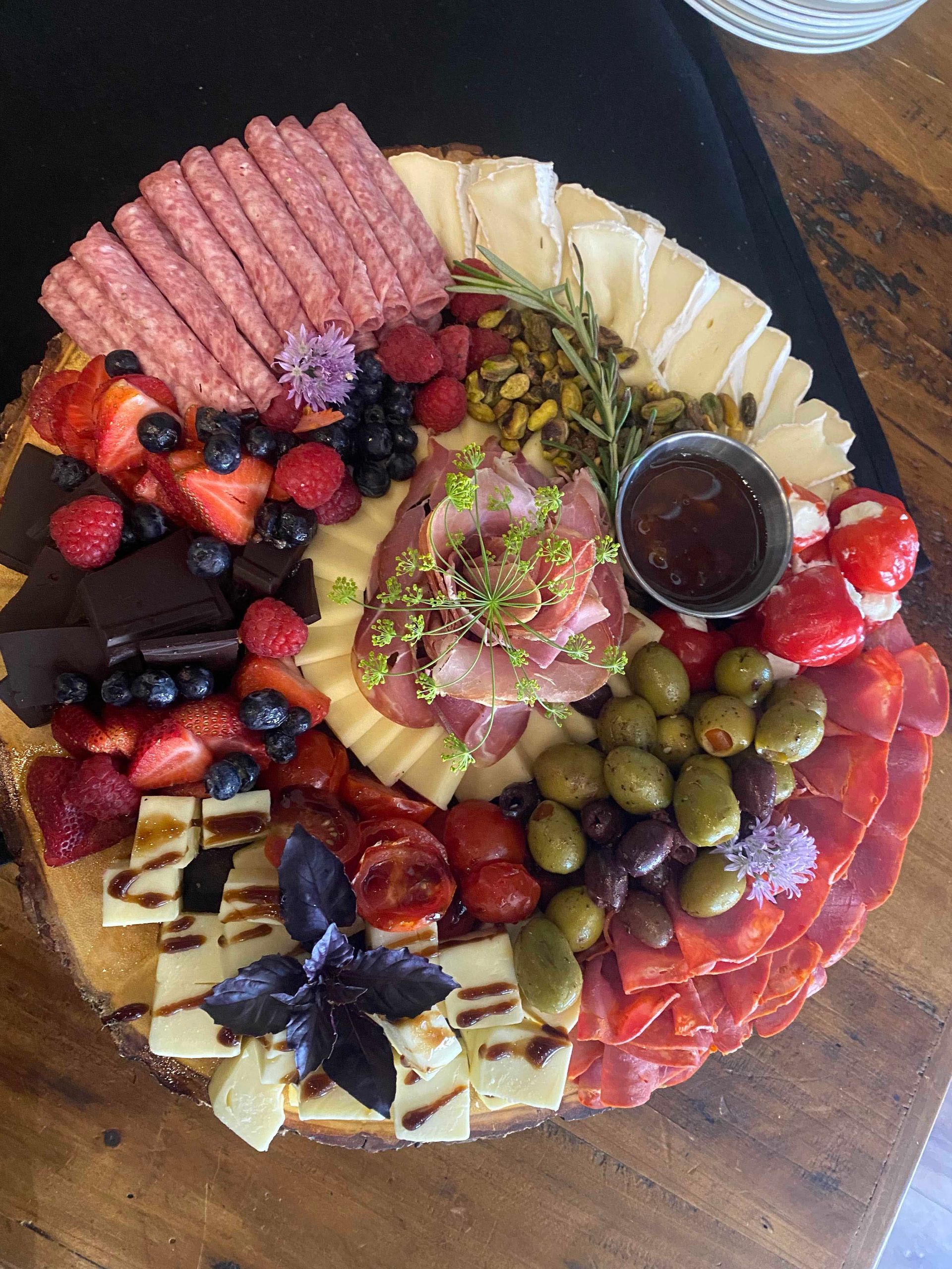 Charcuterie board with cheeses, meats, fruits, olives, and a small dish of jam.