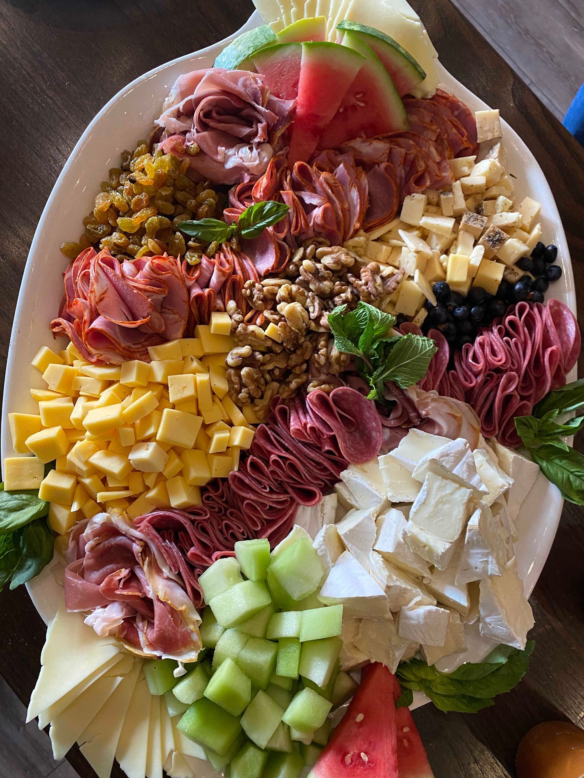 Oval platter with charcuterie: meats, cheeses, watermelon, melon, nuts, and olives.