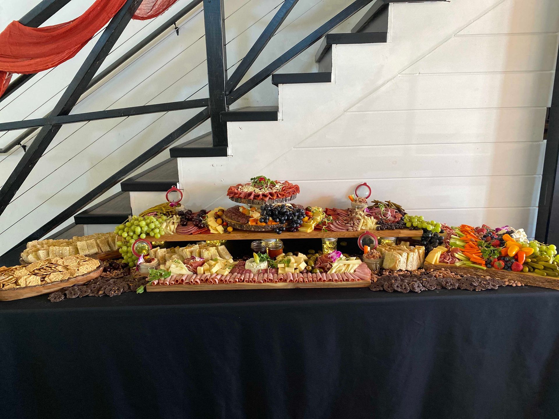 Charcuterie board with cheeses, meats, grapes, and crackers on a black table with stairs in the background.