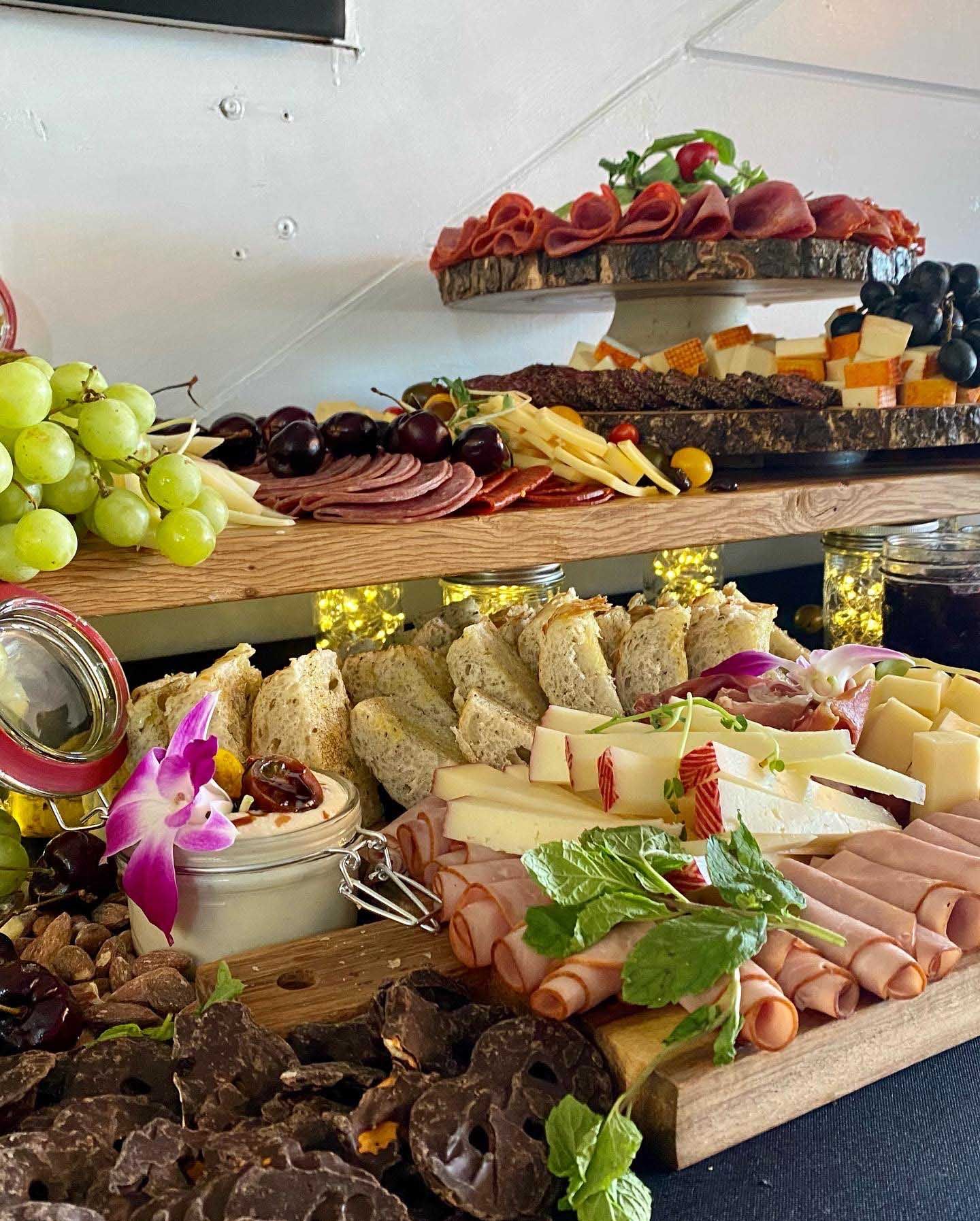 Charcuterie board with meats, cheeses, grapes, and breads on wooden platters.