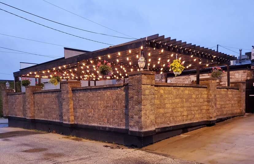 Outdoor patio with string lights, brick wall, and hanging flower baskets.
