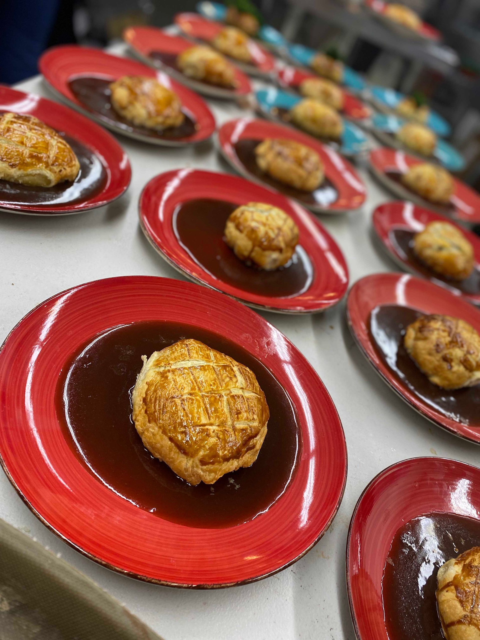 Plates of puff pastry-topped food in brown sauce on red plates, prepared for serving.