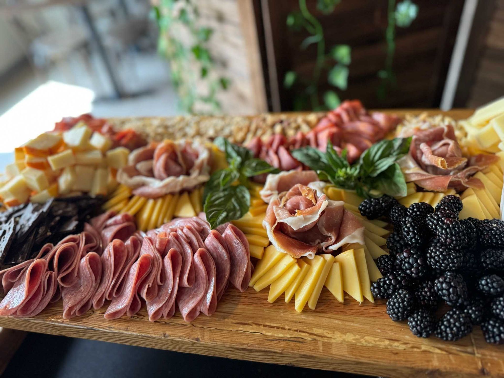 Wooden charcuterie board with sliced meats, cheeses, blackberries, and basil.