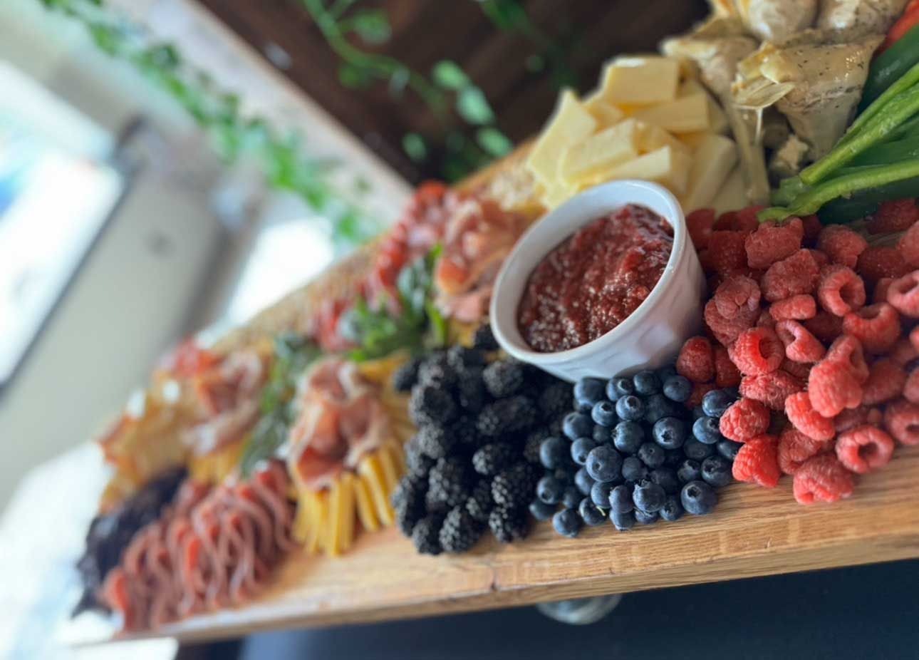 Charcuterie board with various foods, including berries, cheese, meat, and jam.