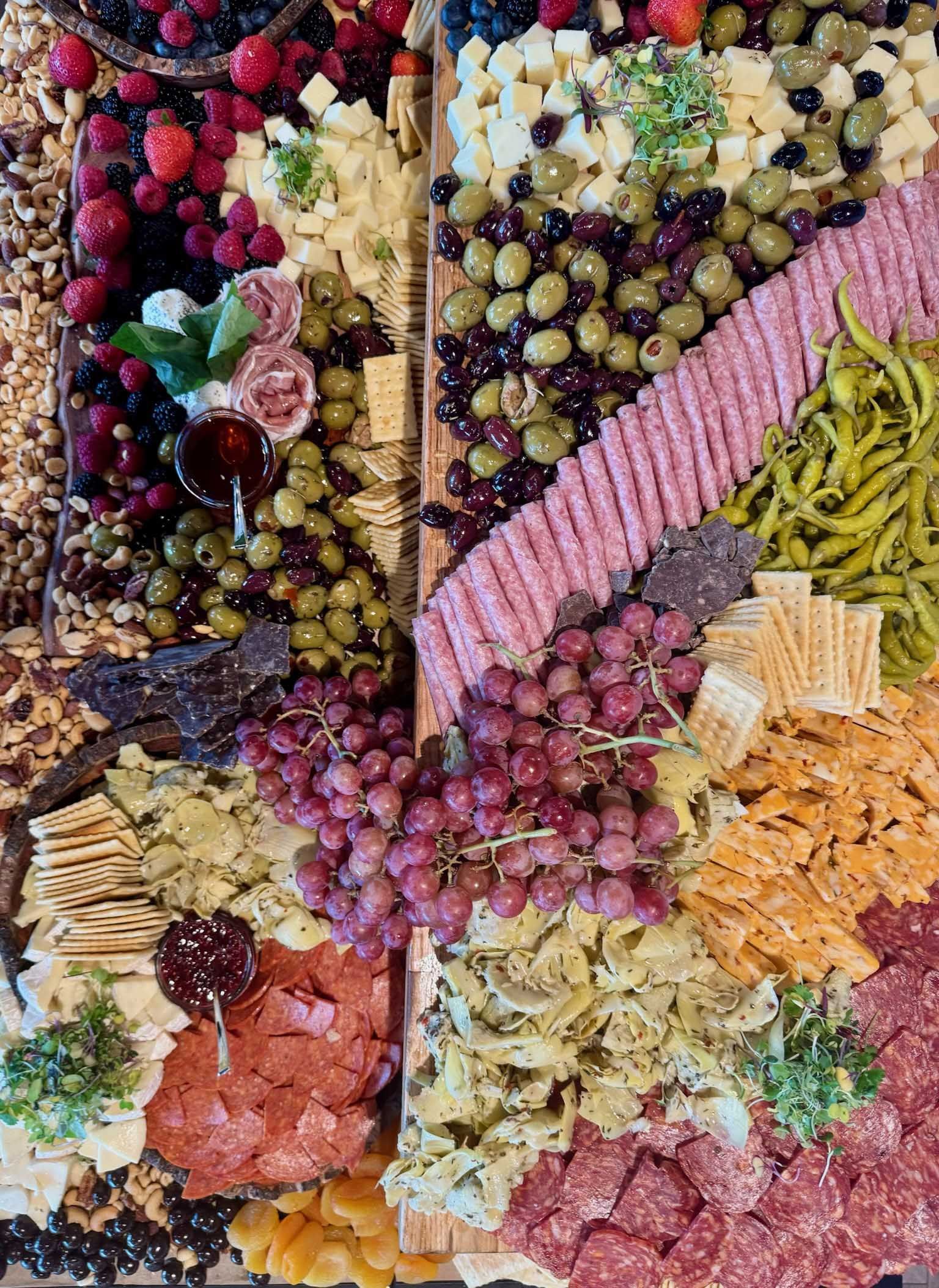 Charcuterie board with a variety of foods: berries, cheese, grapes, olives, crackers, and meats.