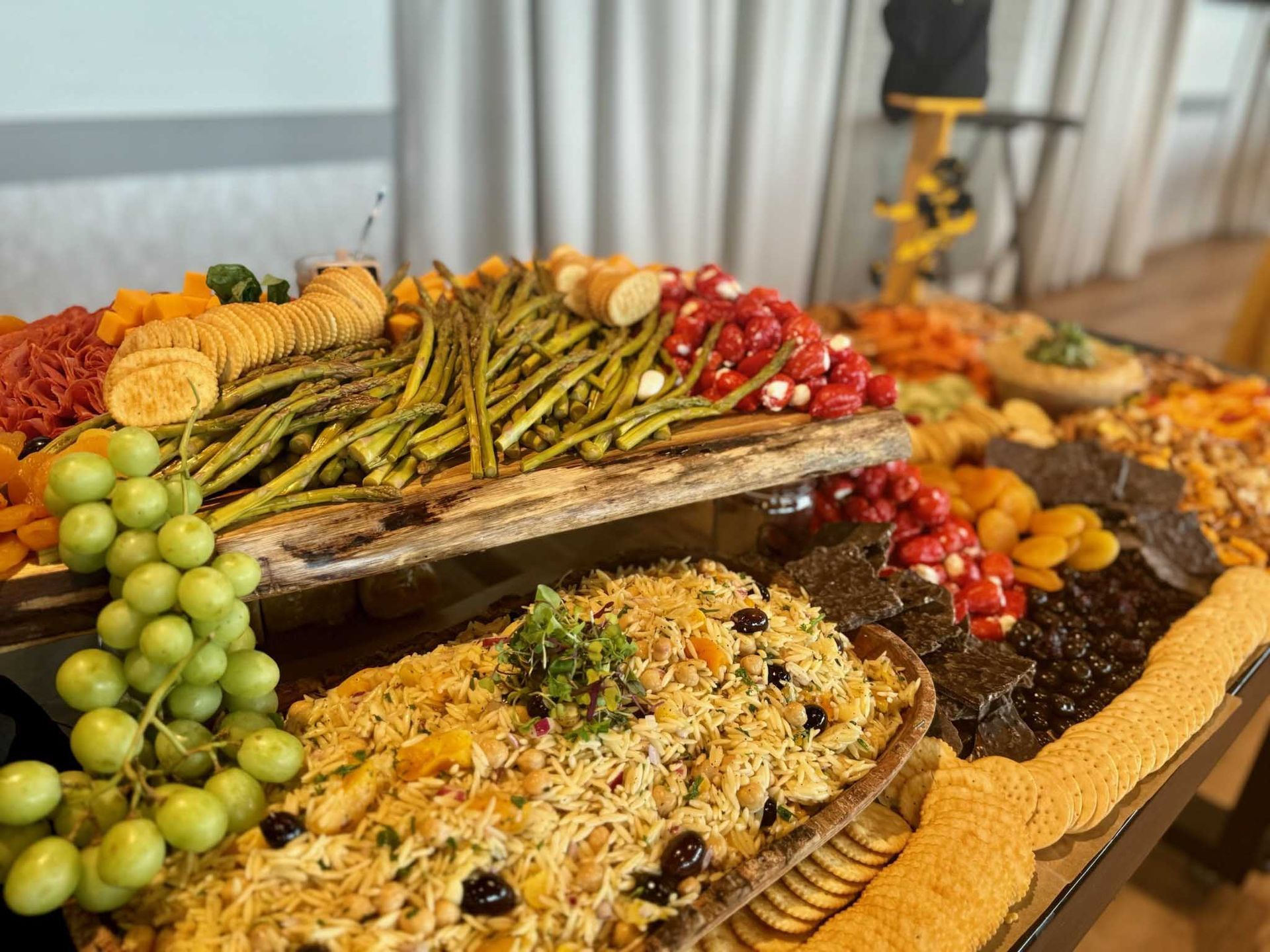 Charcuterie board with asparagus, grapes, dried apricots, rice, and crackers.