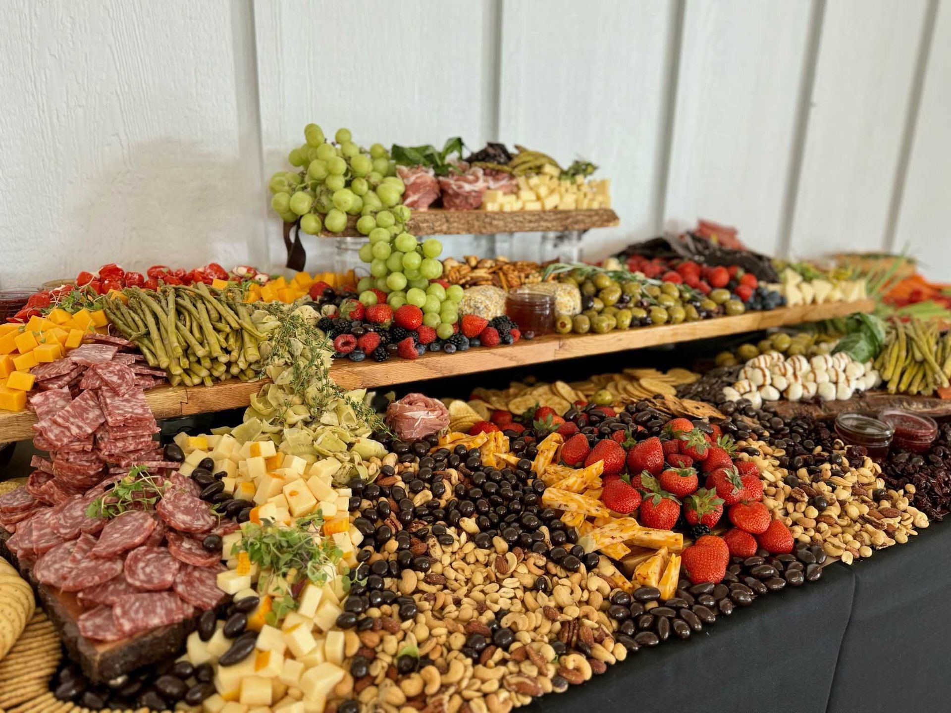 Charcuterie board overflowing with cheeses, fruits, nuts, olives, and meats on a black-covered table.