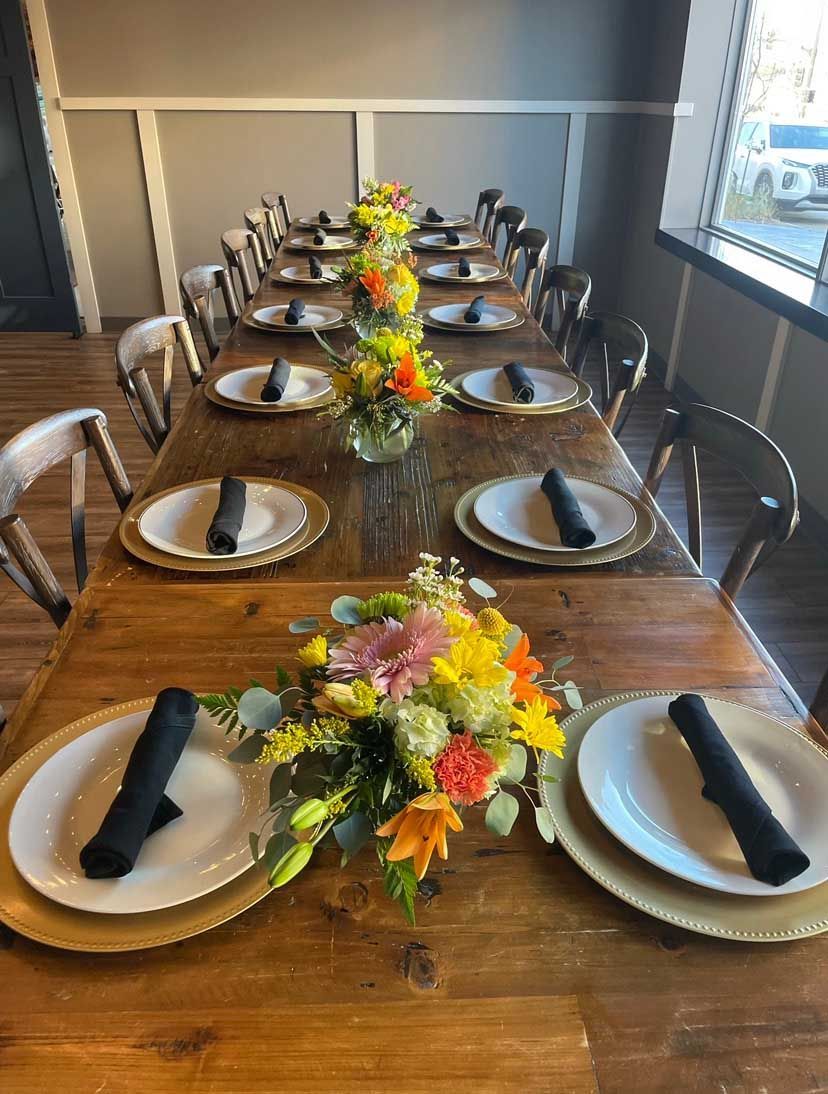 Long wooden table set for a meal with plates, napkins, and floral centerpieces.