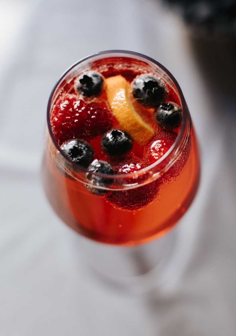 Red cocktail in a glass, garnished with blueberries and a citrus slice.