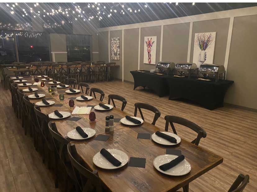 Long wooden tables set for a meal in a room with food service stations.