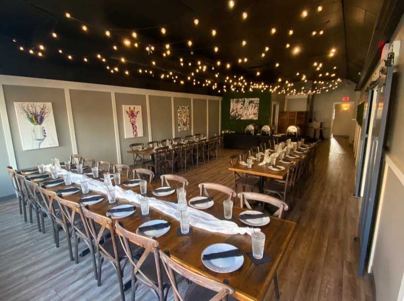Dining room with long wooden tables set for a meal. String lights hang from a black ceiling.