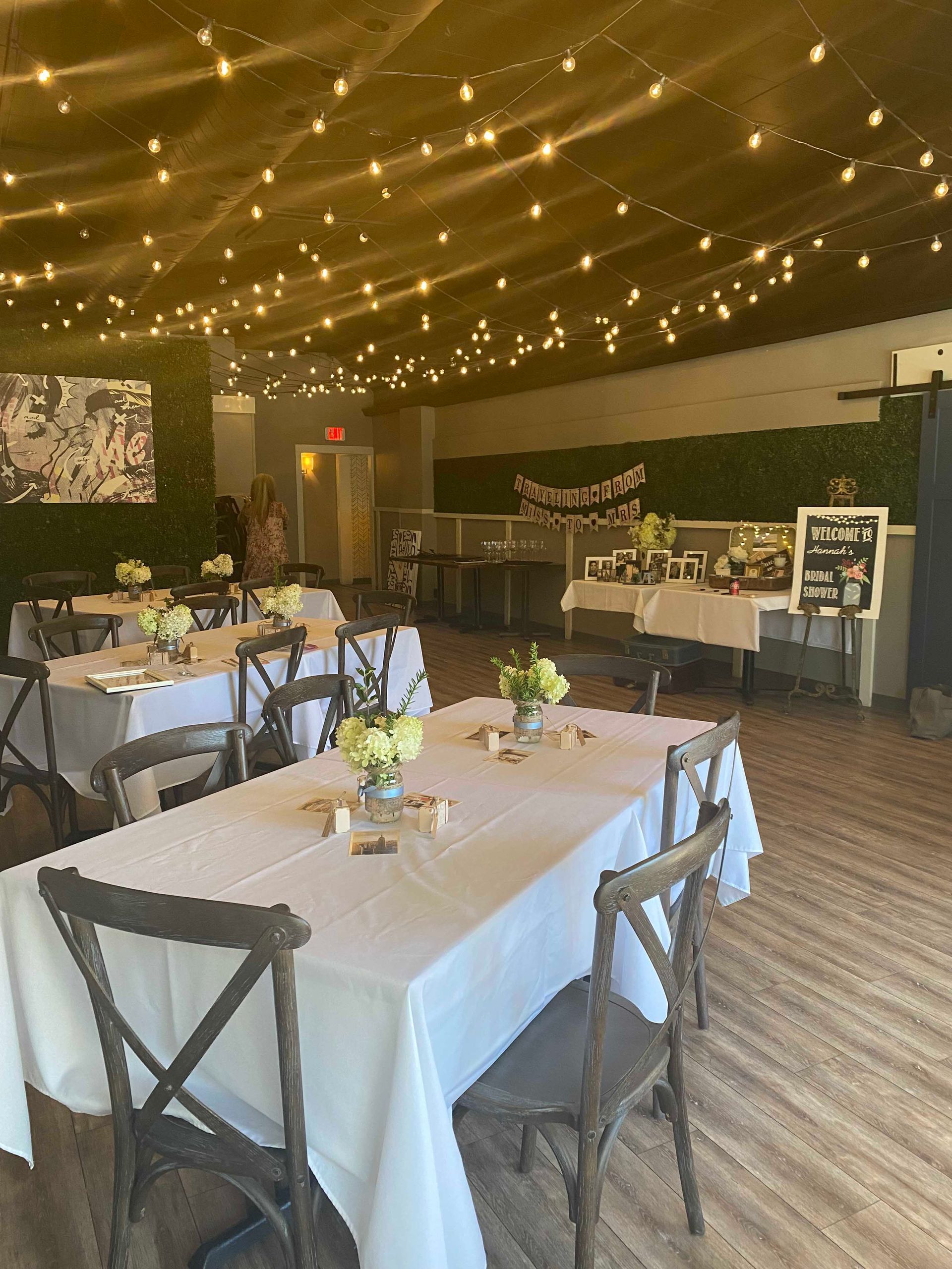 Event space with tables, chairs, decorations, and string lights overhead.