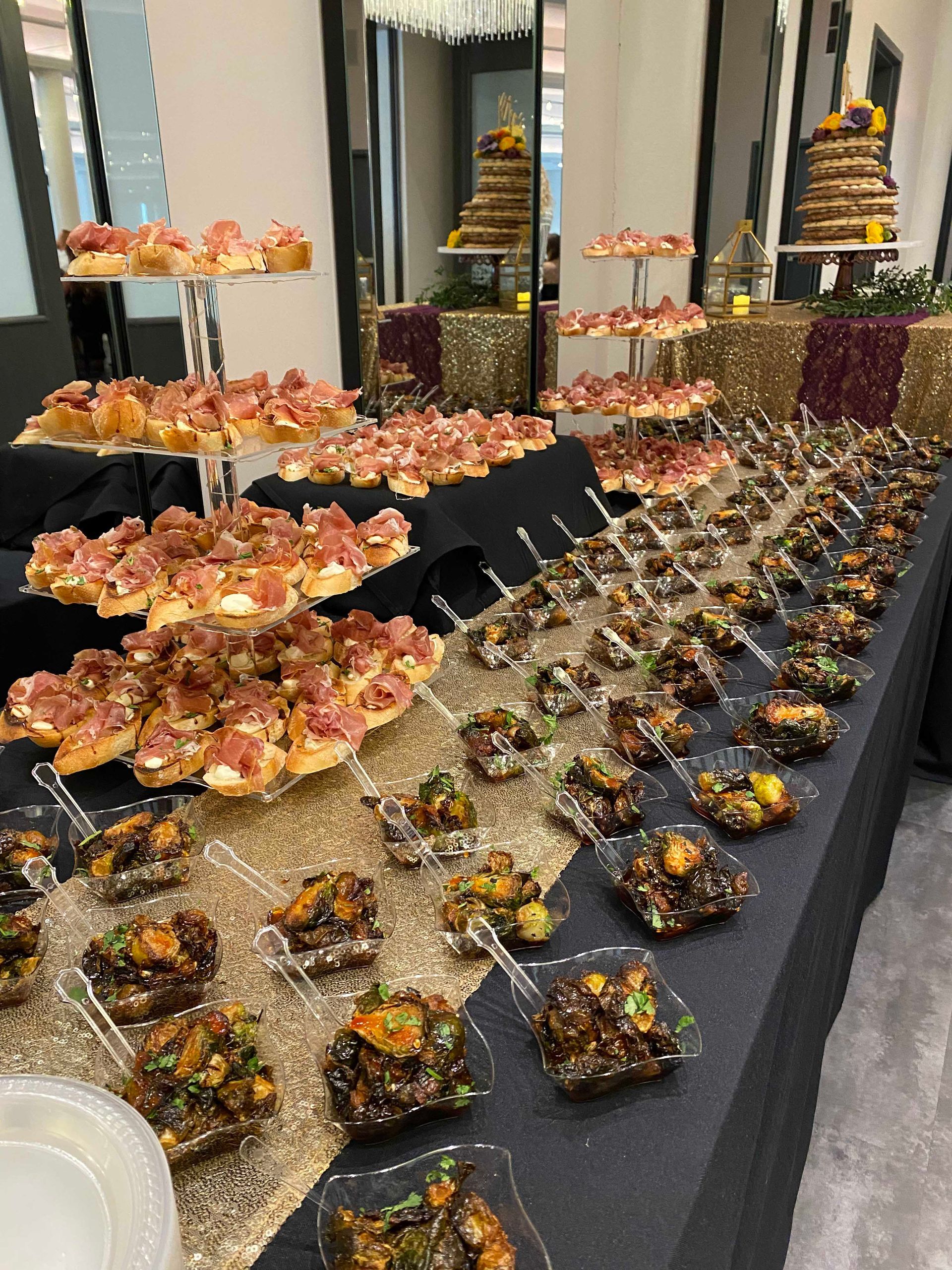 A buffet table with various appetizers and desserts, including bruschetta, on black and gold linens.