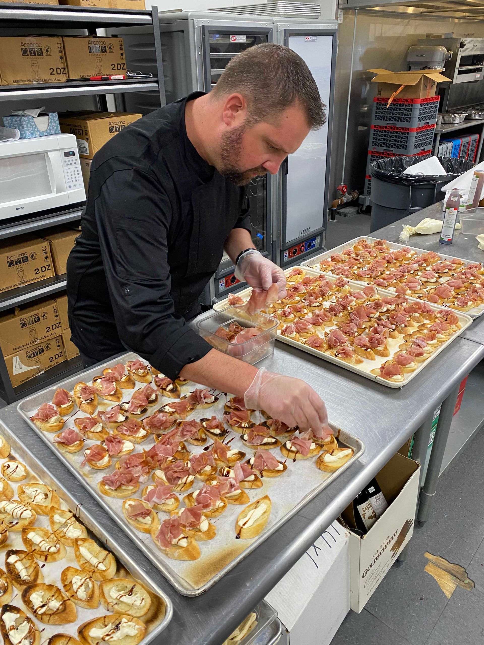 Chef arranging appetizers on trays in a commercial kitchen.