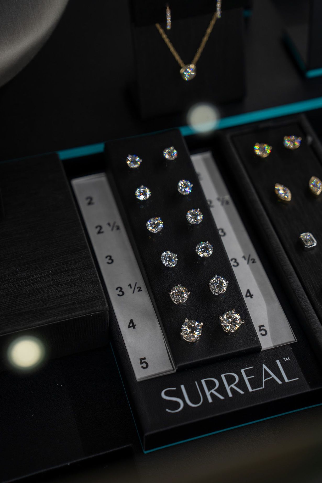 Black jewelry display with sparkling earrings, a ruler, and the word “SURREAL” on the base.