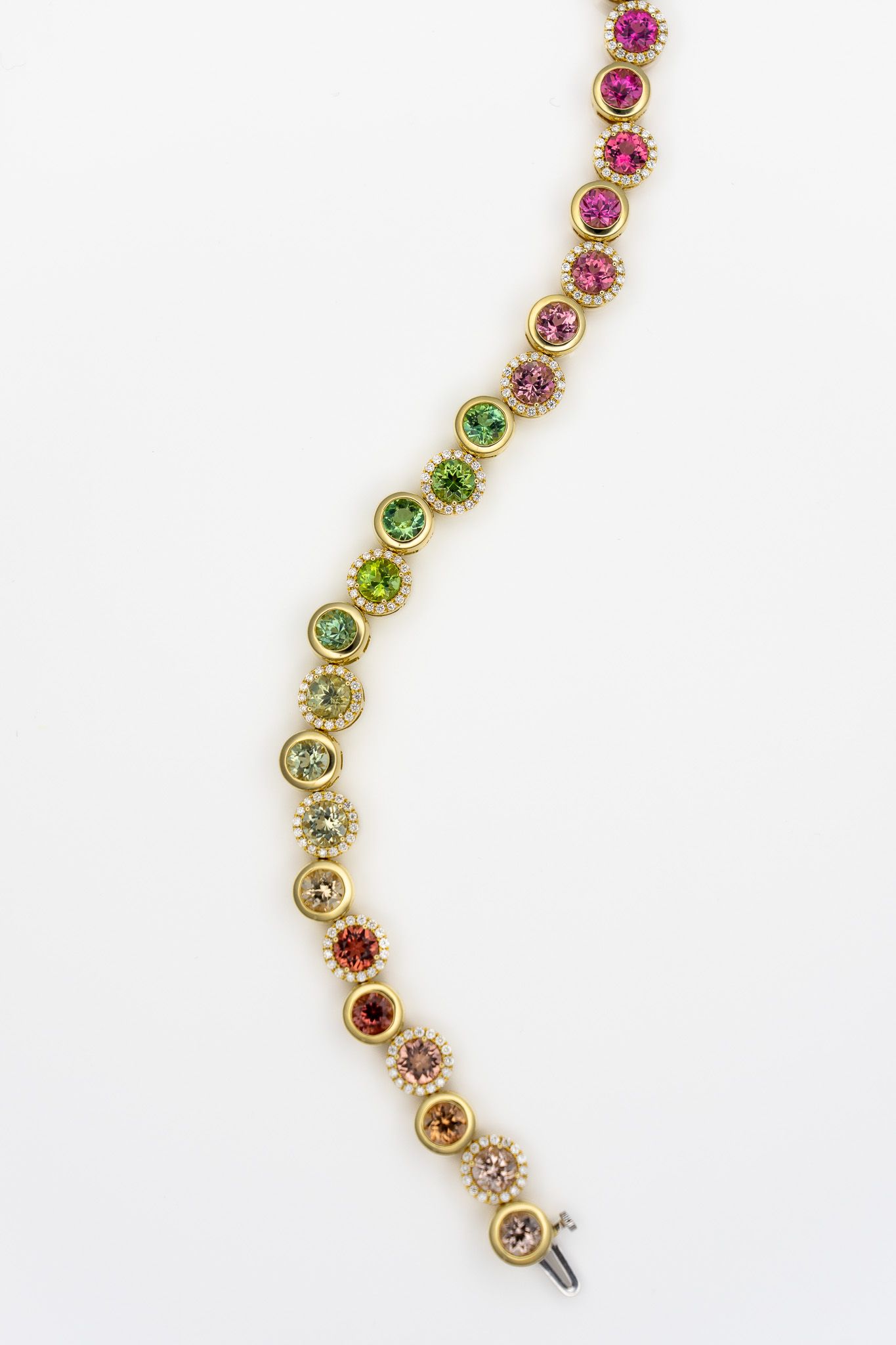 Gold bracelet with colorful gemstone circles in pink, green, red, and clear stones on a white background.
