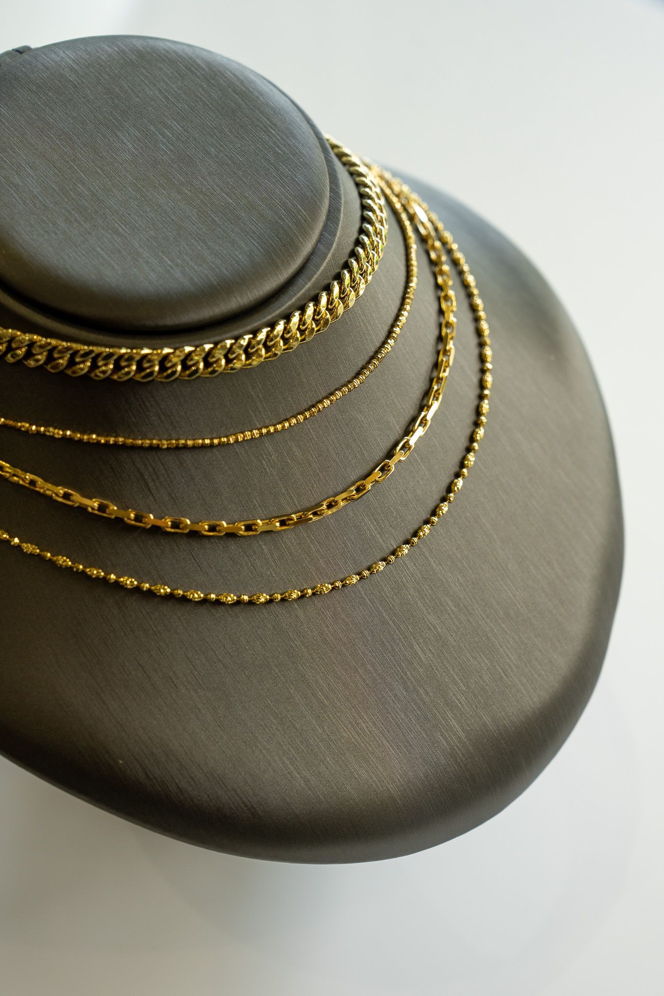 Gold chain necklaces on a gray velvet display bust.